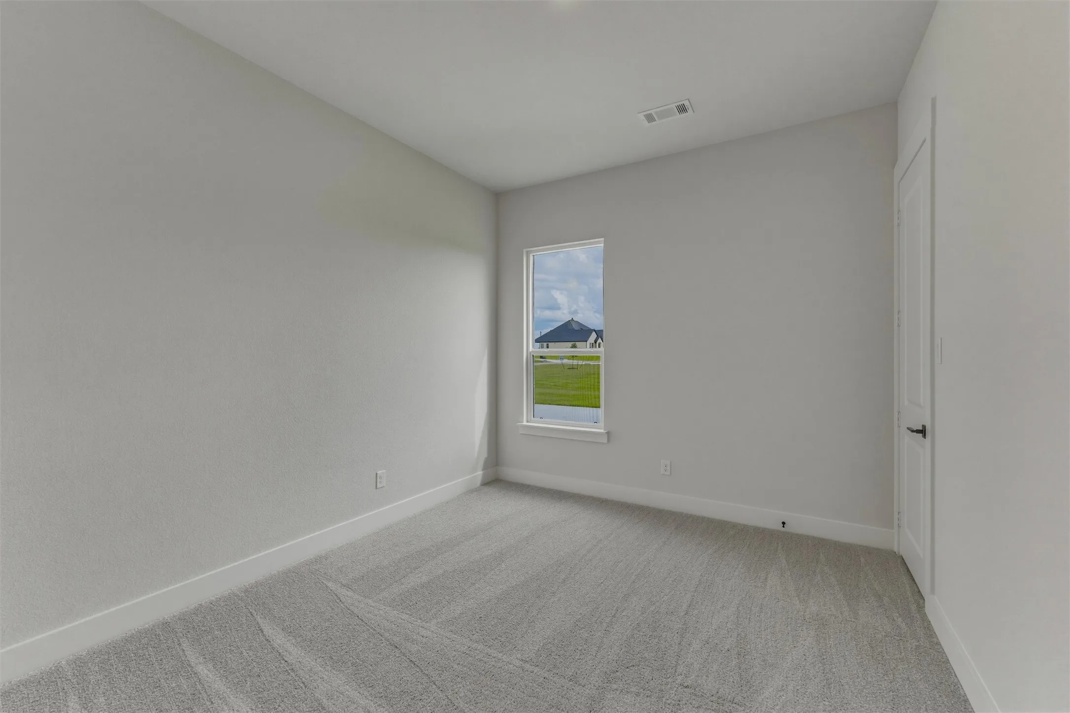 Bright room featuring a single window, light gray carpet flooring, white baseboards, and a white paneled door with a black handle