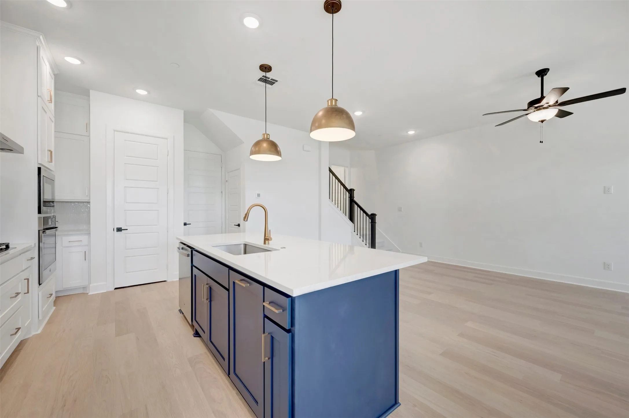 Modern kitchen featuring a blue island with a built-in sink and gold-tone faucet, complemented by white cabinetry and stainless steel appliances