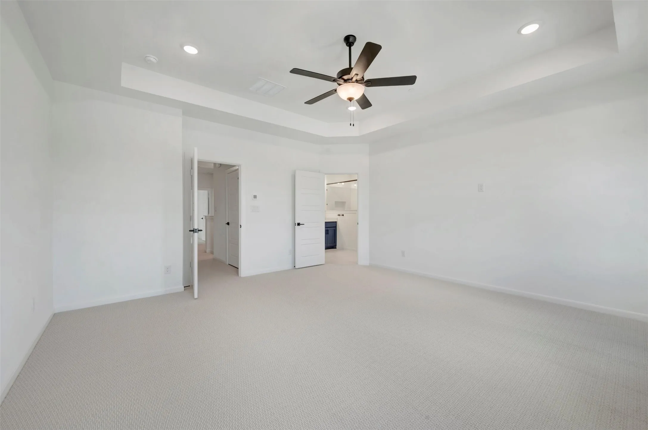 Spacious room featuring light-colored carpeting, a tray ceiling, and recessed lighting