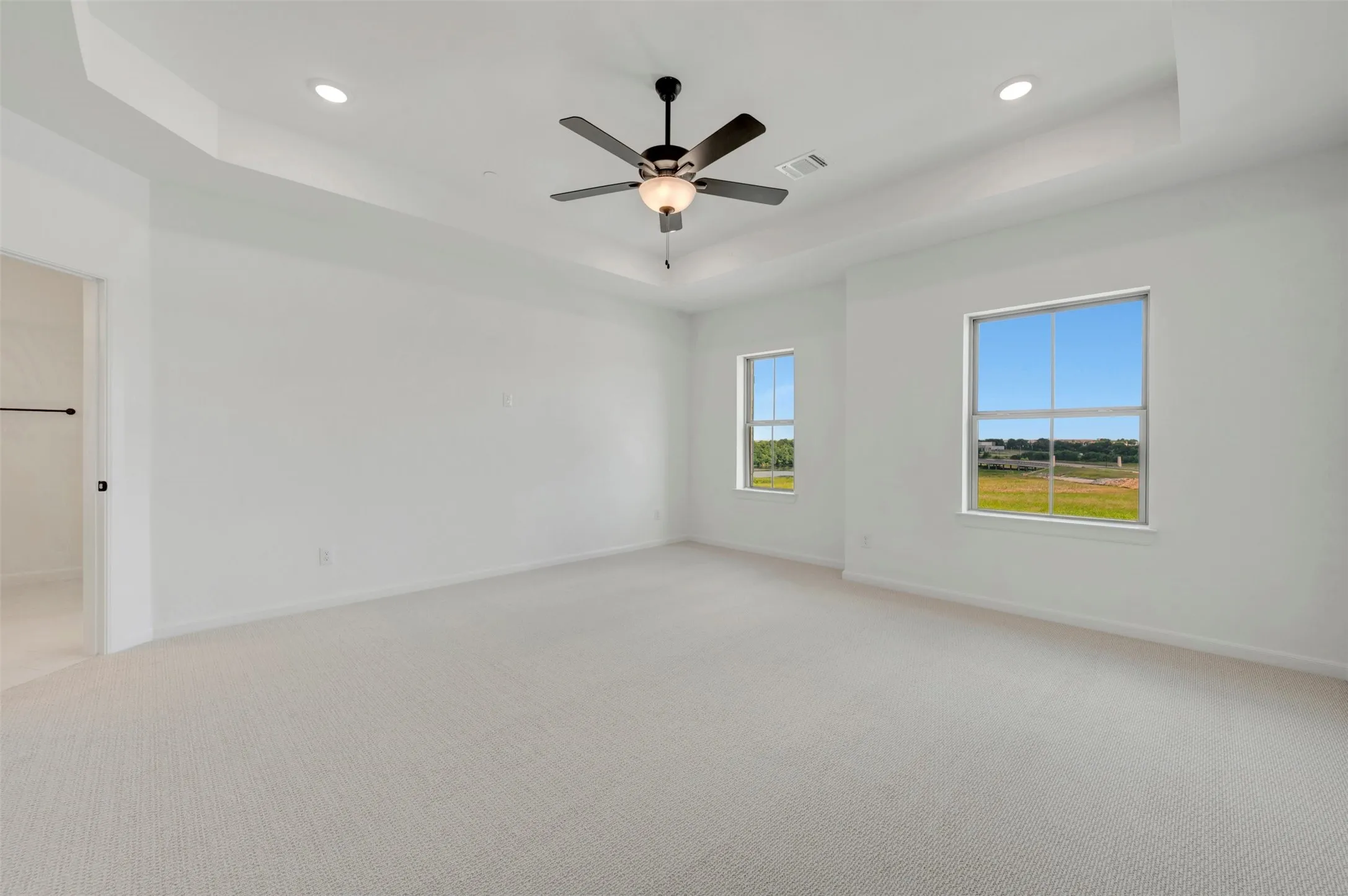 Spacious room featuring tray ceilings with recessed lighting, a ceiling fan, and light-toned carpeting