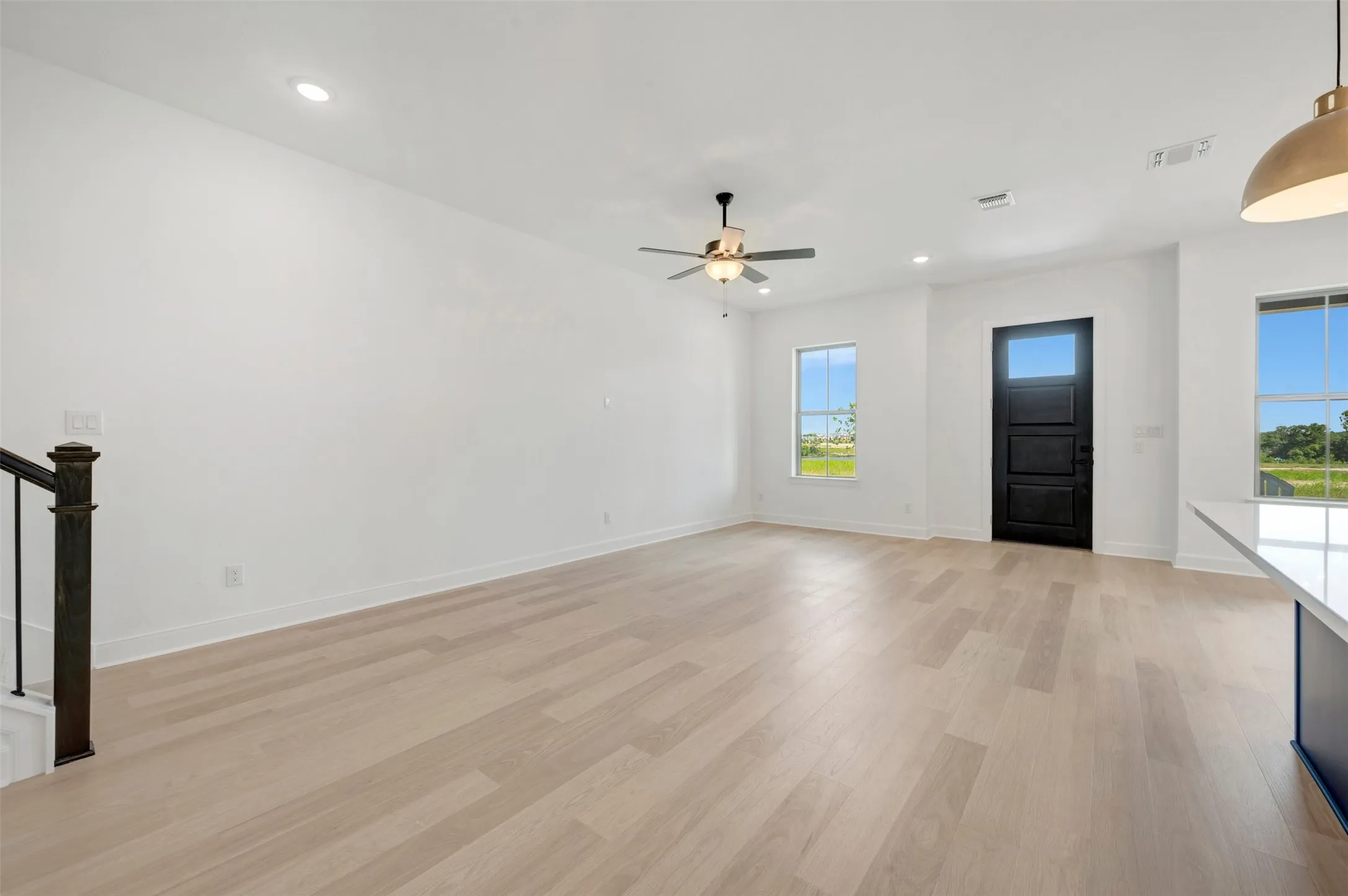 Spacious living area featuring light wood-finish flooring, recessed lighting, and a ceiling fan