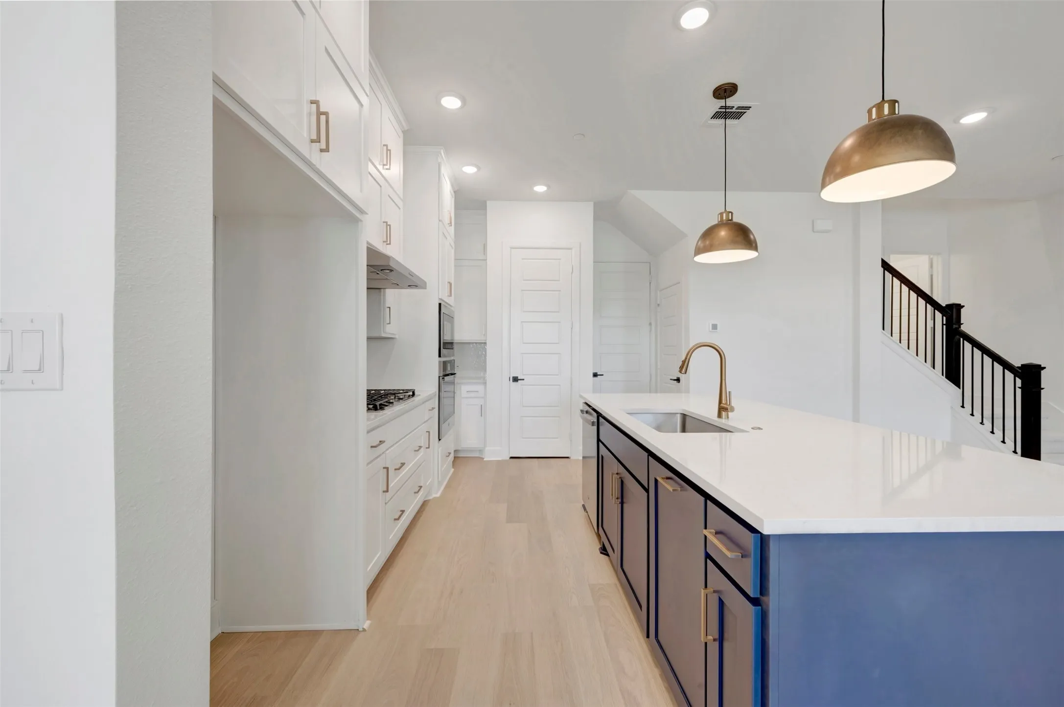 Kitchen featuring a blue-paneled island with a white countertop and gold-toned fixtures, light wood-finish flooring, white cabinetry with gold-toned hardware, recessed lighting, and a stainless steel wall oven