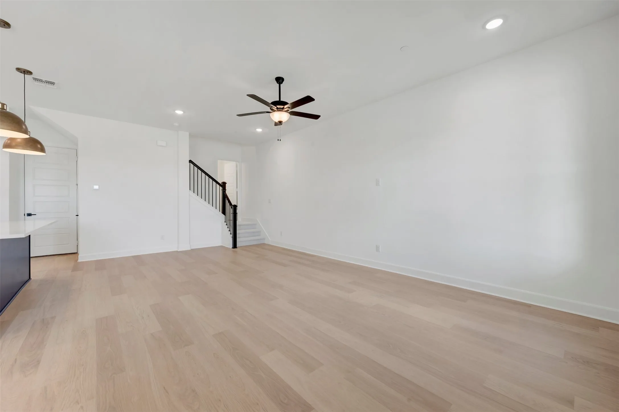 Spacious living area featuring light wood-finish flooring, white walls, and recessed lighting