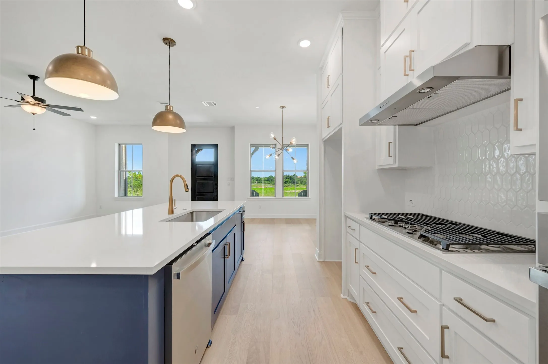 Contemporary kitchen featuring a large central island with a sink and gold-tone faucet, white countertops, built-in dishwasher, and a gas range with an overhead vent hood
