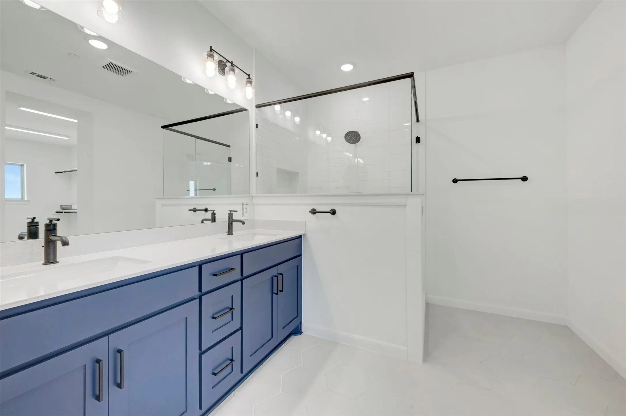Contemporary bathroom featuring dual blue vanity with black hardware, white countertops, dual undermount sinks with black fixtures, and a glass-enclosed shower with black framing