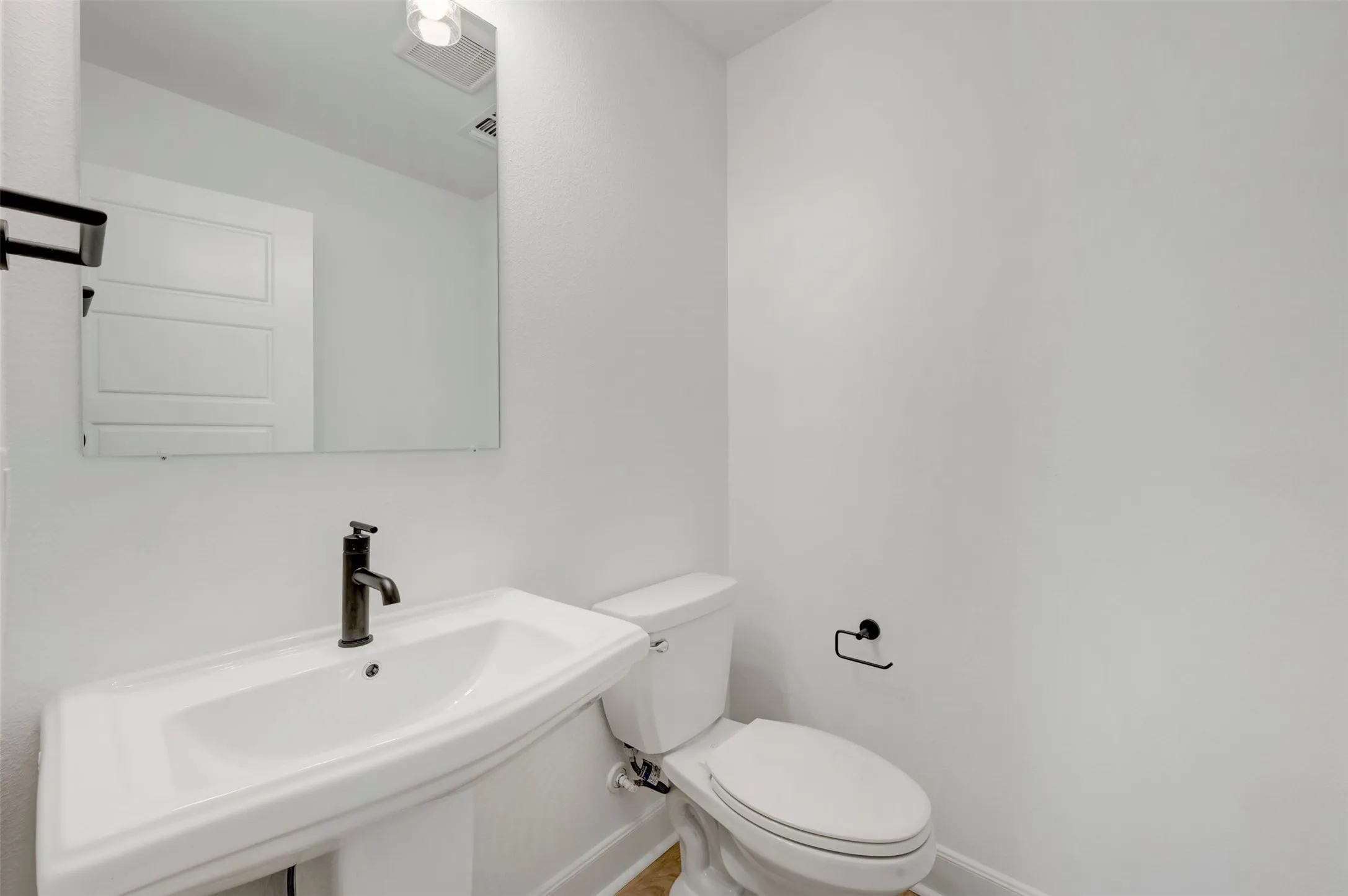 Pedestal sink with dark bronze faucet, wall-mounted mirror, and white toilet with dark bronze toilet paper holder