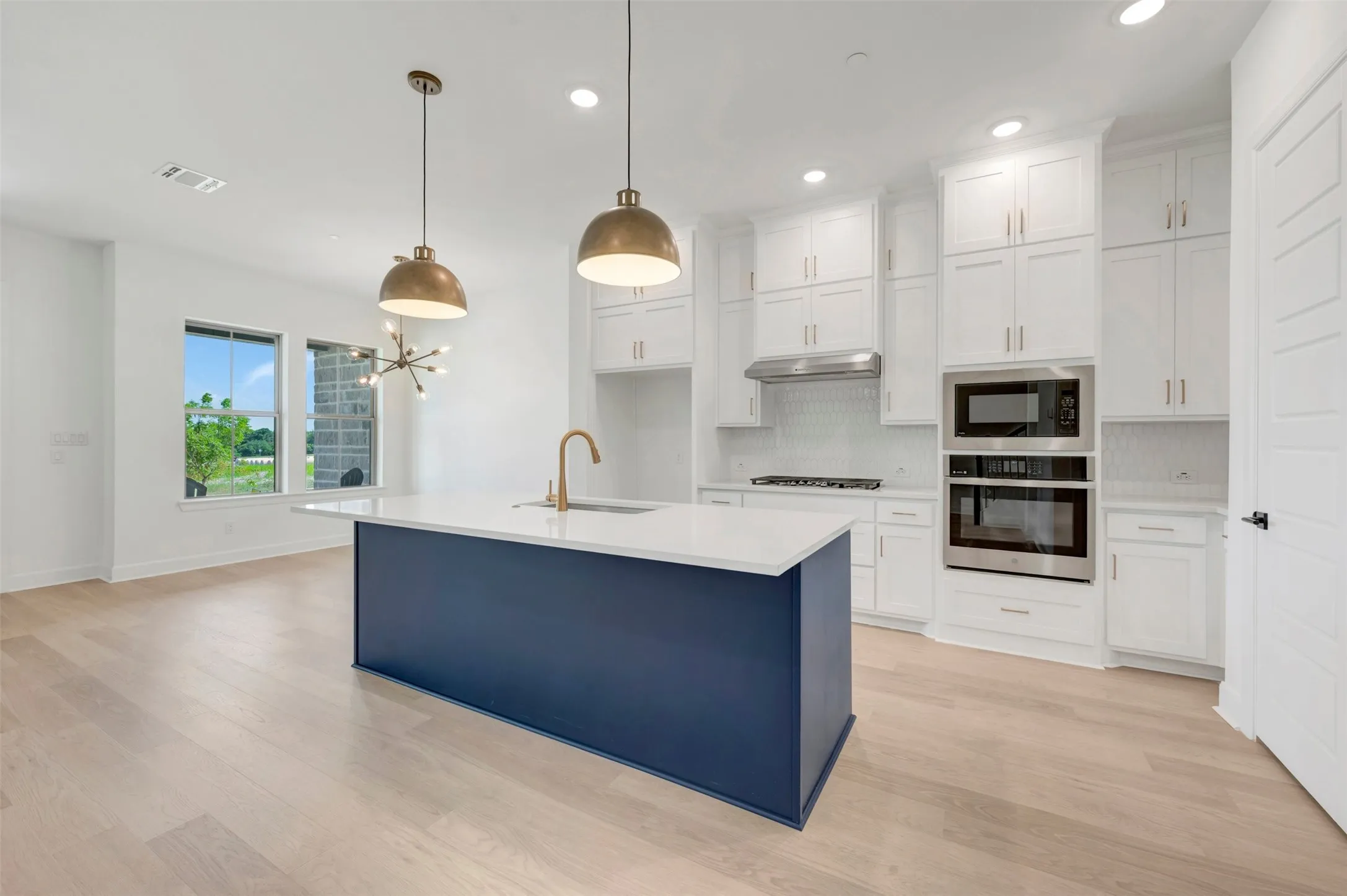 Bright kitchen featuring a blue island with a white countertop and brass-finish faucet, white cabinetry, stainless steel appliances, and wood-finish flooring