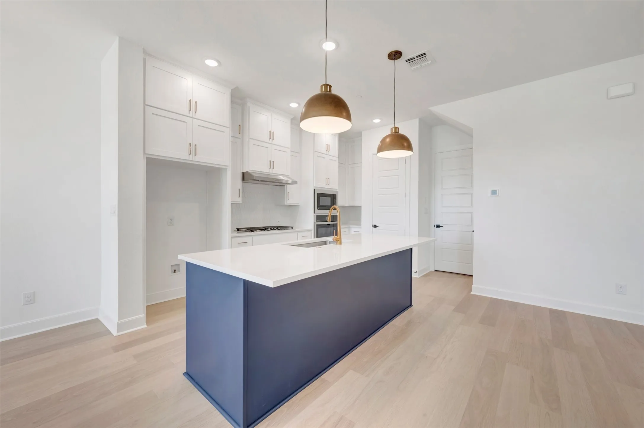 Open-concept kitchen featuring a navy island with a white countertop, brass pendant lighting, light wood-finish flooring, white cabinetry, and recessed lighting