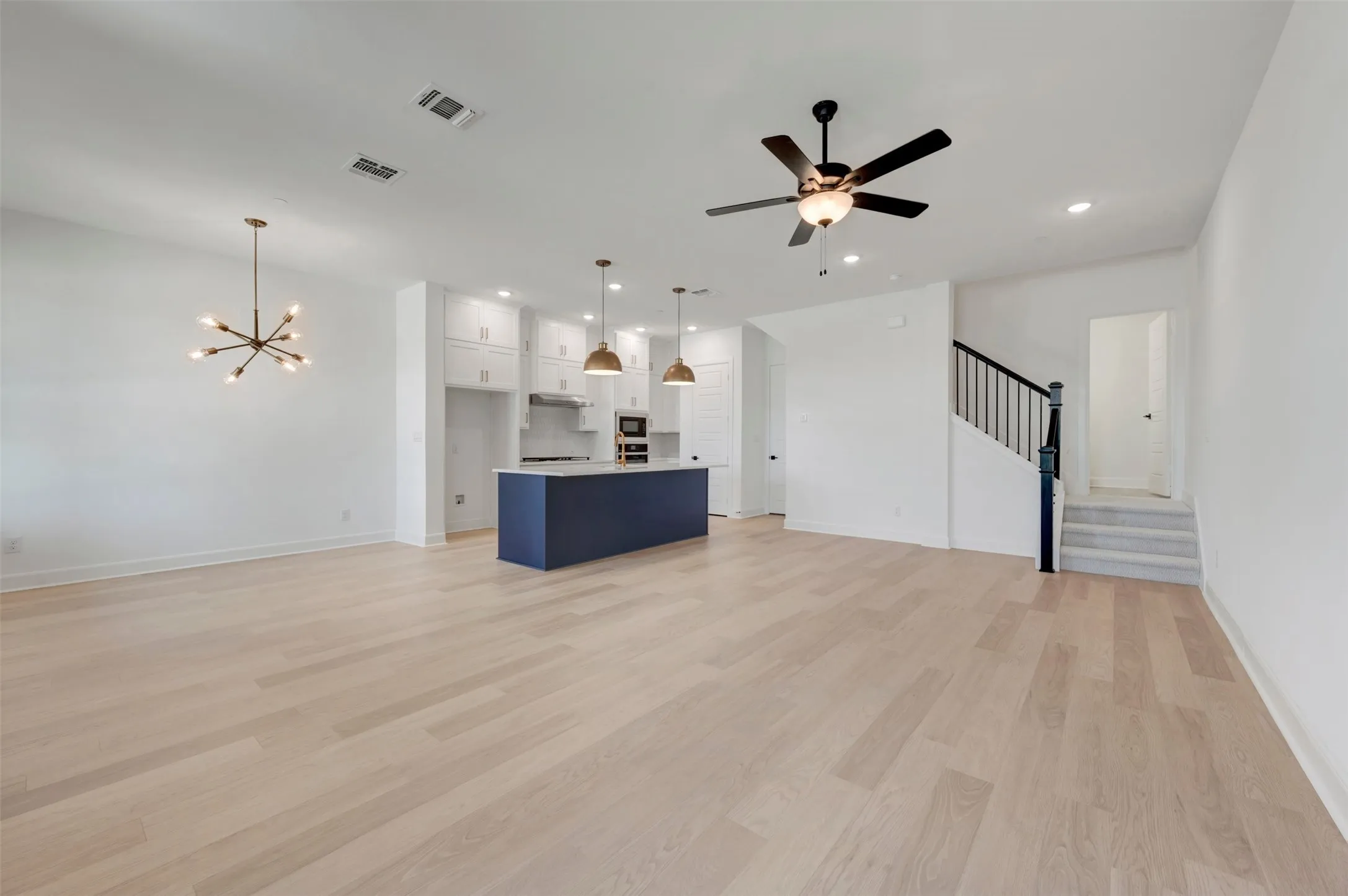 Open-concept living space featuring wood-finish flooring, a contemporary chandelier, and a ceiling fan
