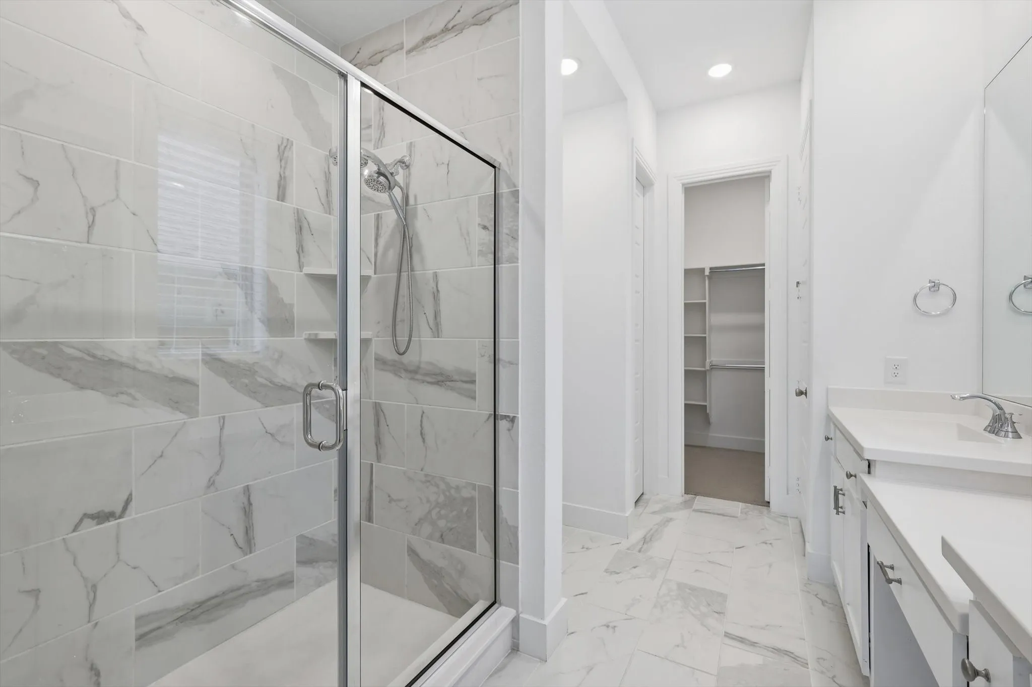 Sleek white cabinetry with marble ceramic tile, oversized walk in shower, dual sinks and make up vanity with natural light and open concept shelving for decor or storage