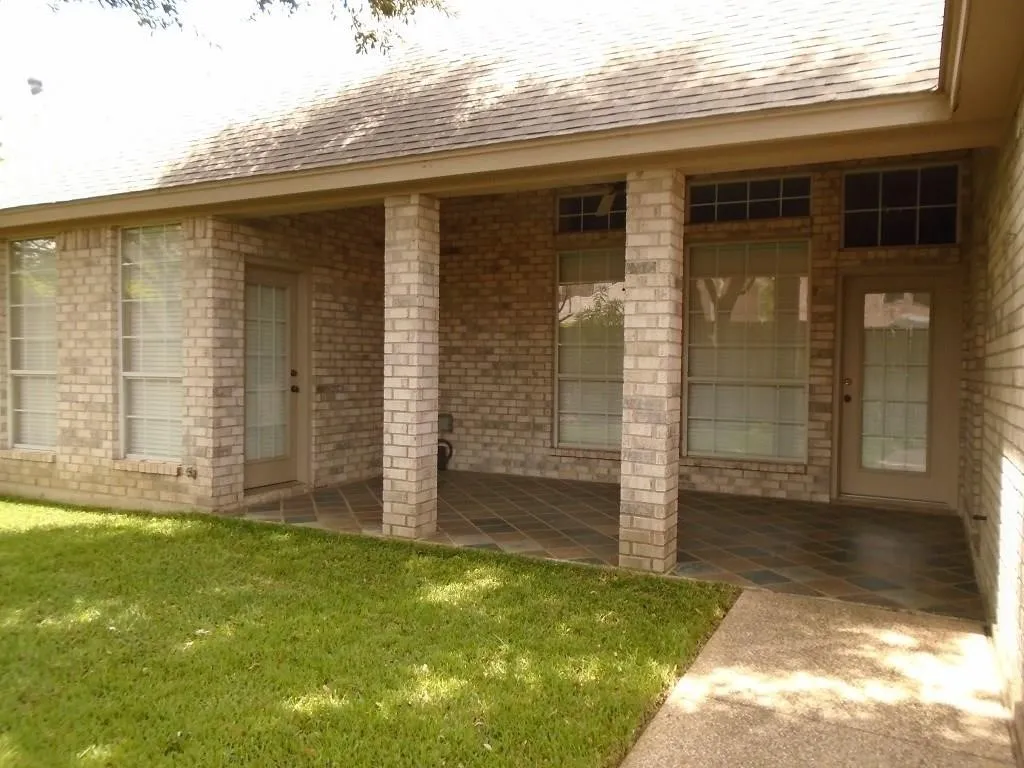 Entrance to property with brick siding, a shingled roof, a patio, and a yard