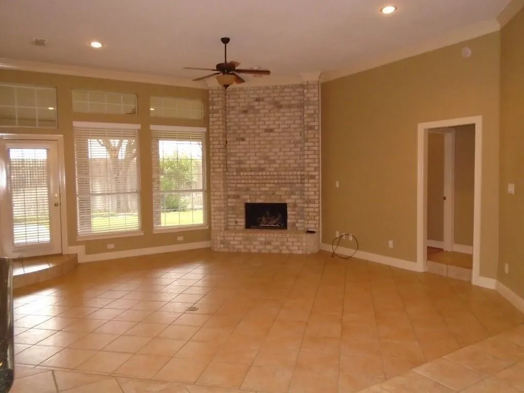 Unfurnished living room with ceiling fan, crown molding, a brick fireplace, light tile patterned floors, and recessed lighting
