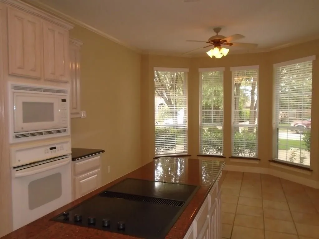 Kitchen with white appliances, crown molding, a ceiling fan, light tile patterned floors, and white cabinetry
