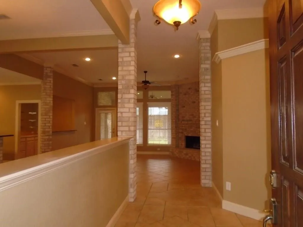 Corridor featuring crown molding, light tile patterned floors, and brick wall