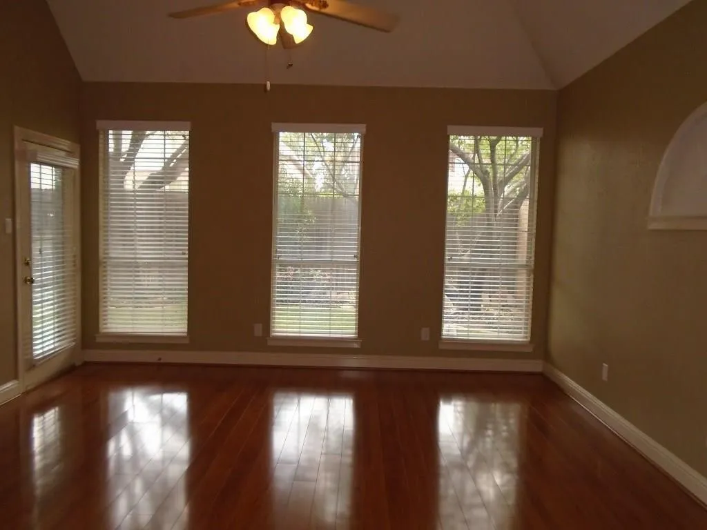 Empty room with vaulted ceiling, ceiling fan, and dark wood-style floors