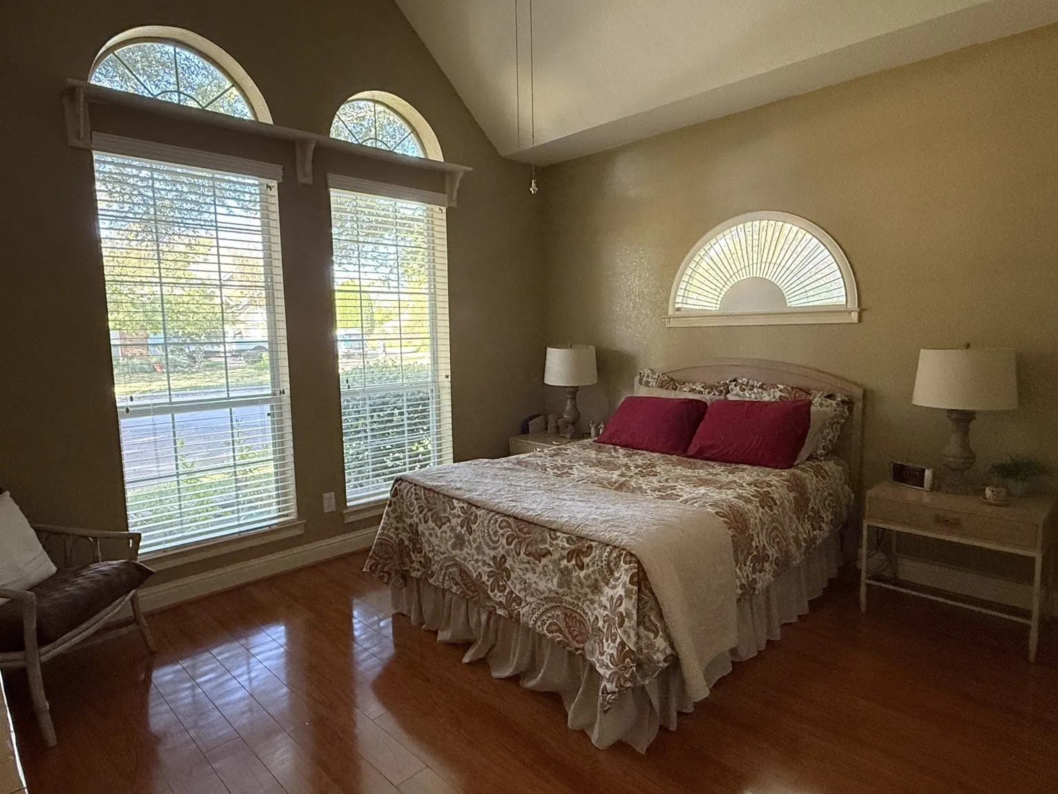 Room featuring vaulted ceiling, hardwood flooring, and multiple windows with arched transoms