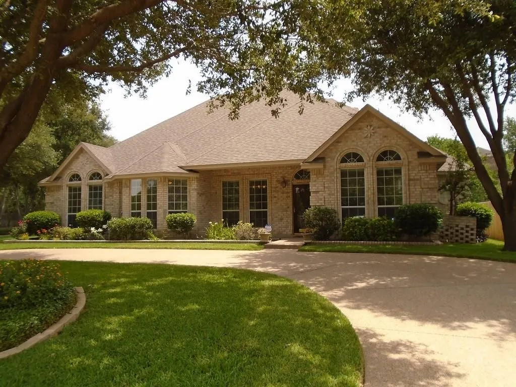 Ranch-style house with a front yard, brick siding, a shingled roof, and covered porch