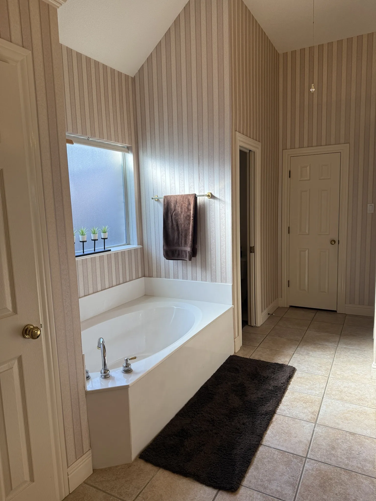 Built-in soaking tub with chrome fixtures, set against striped wallpaper and tile flooring