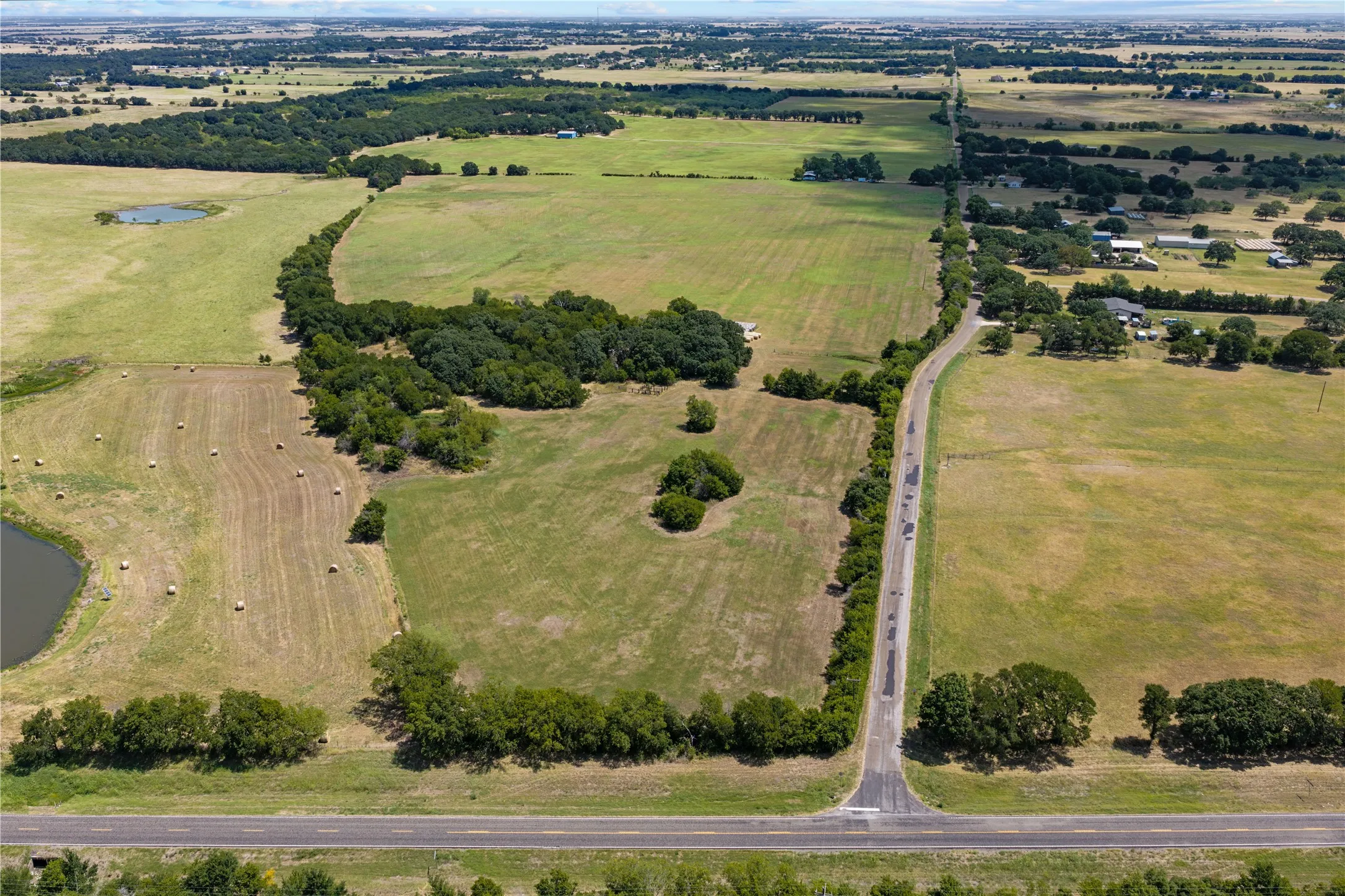 Expansive acreage featuring green fields, mature trees, and a pond