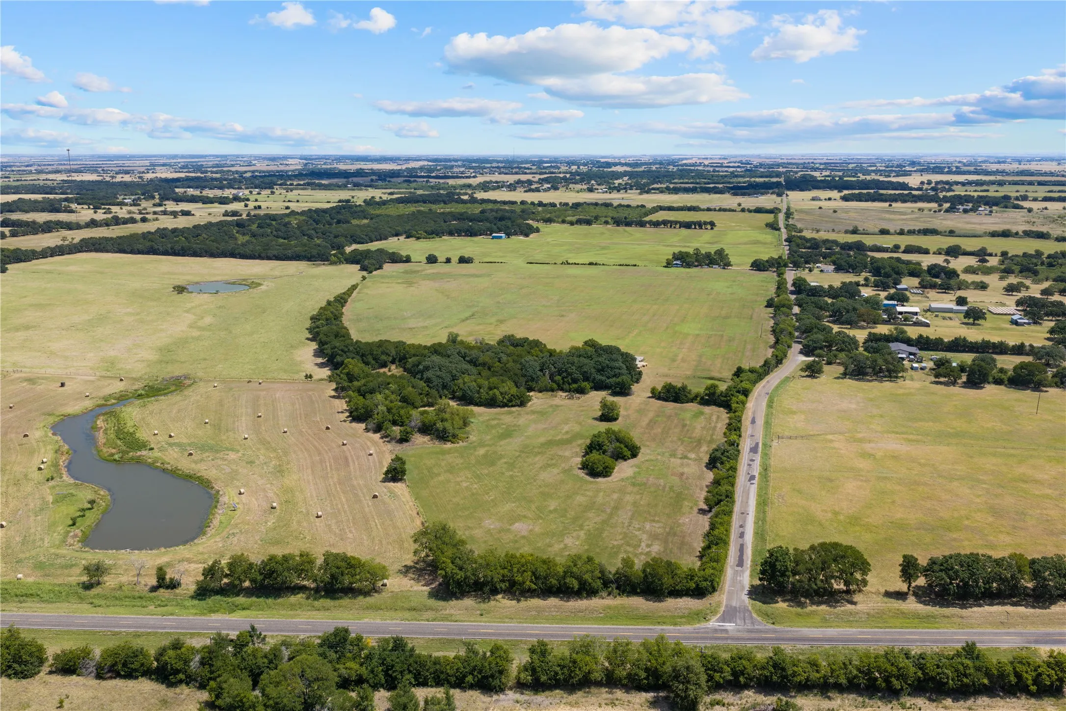 Expansive land parcel featuring a winding roadway, established trees, and two distinct water features