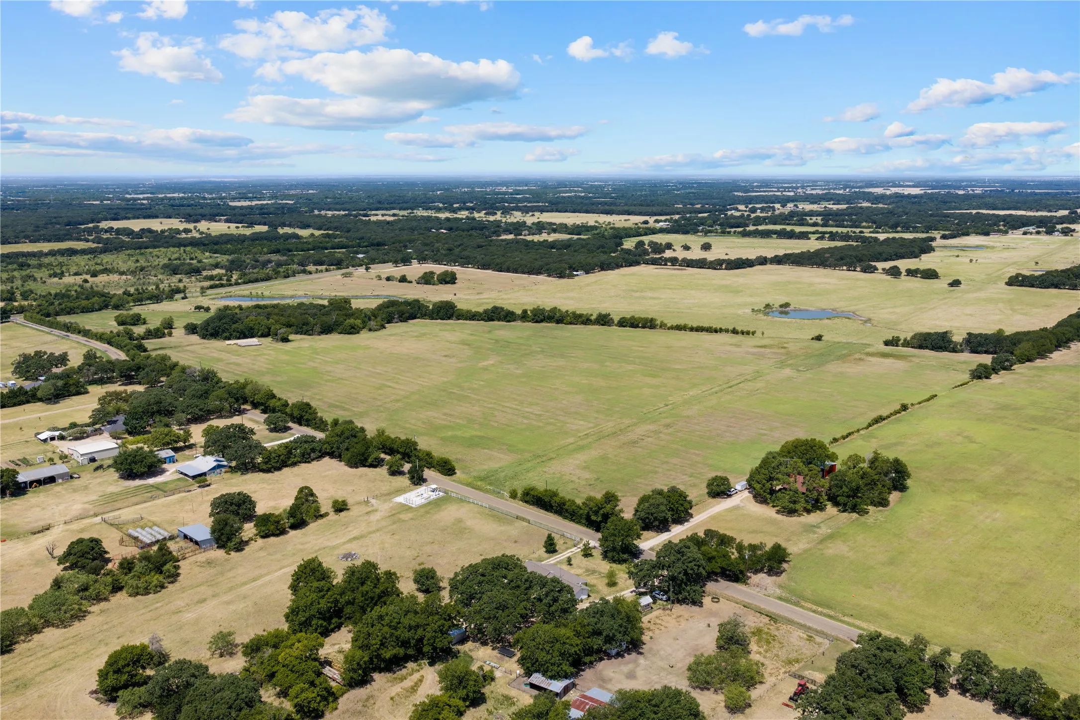 Expansive landscape featuring open fields, scattered mature trees, and a visible pond