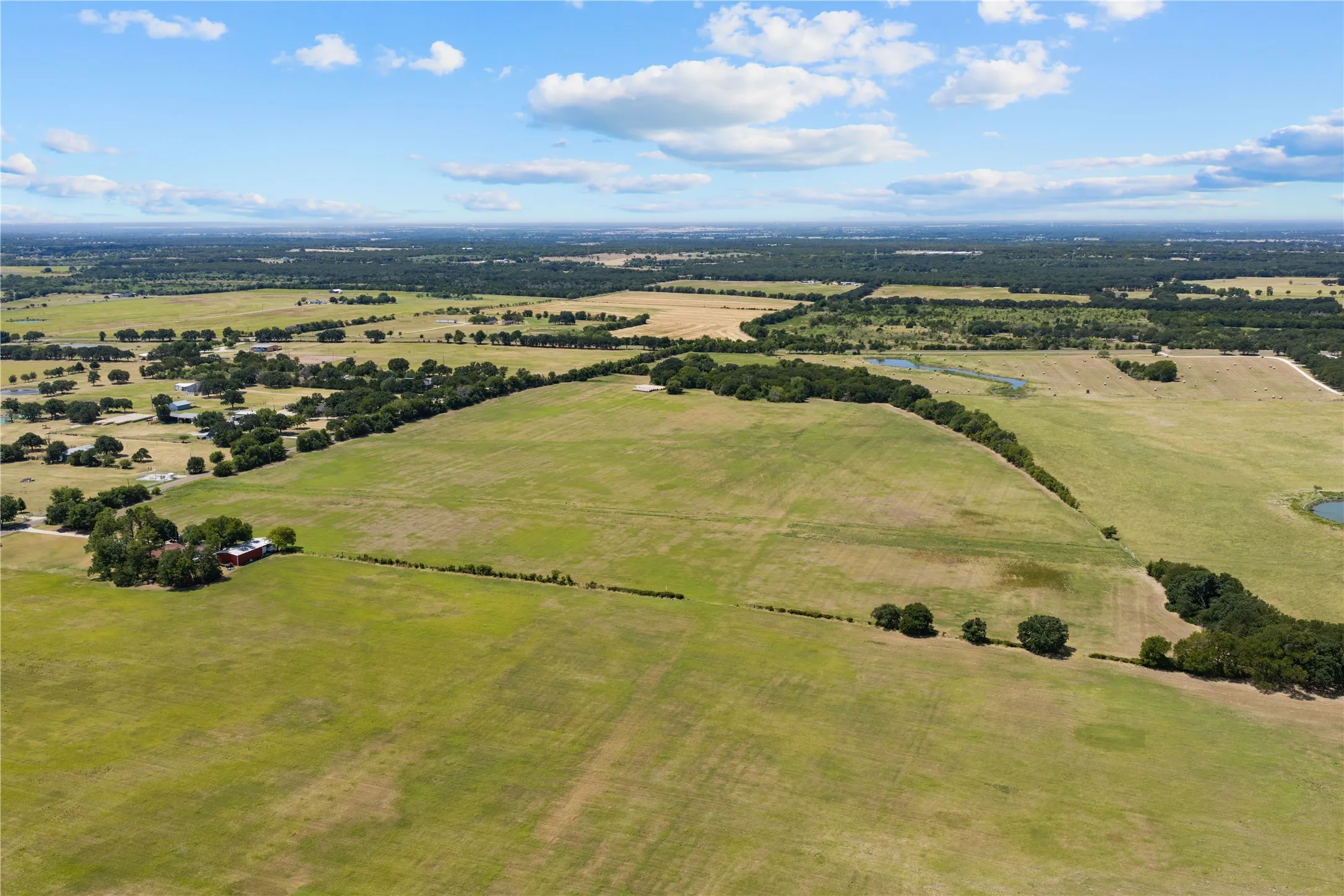 Expansive green acreage with scattered mature trees and distant water features