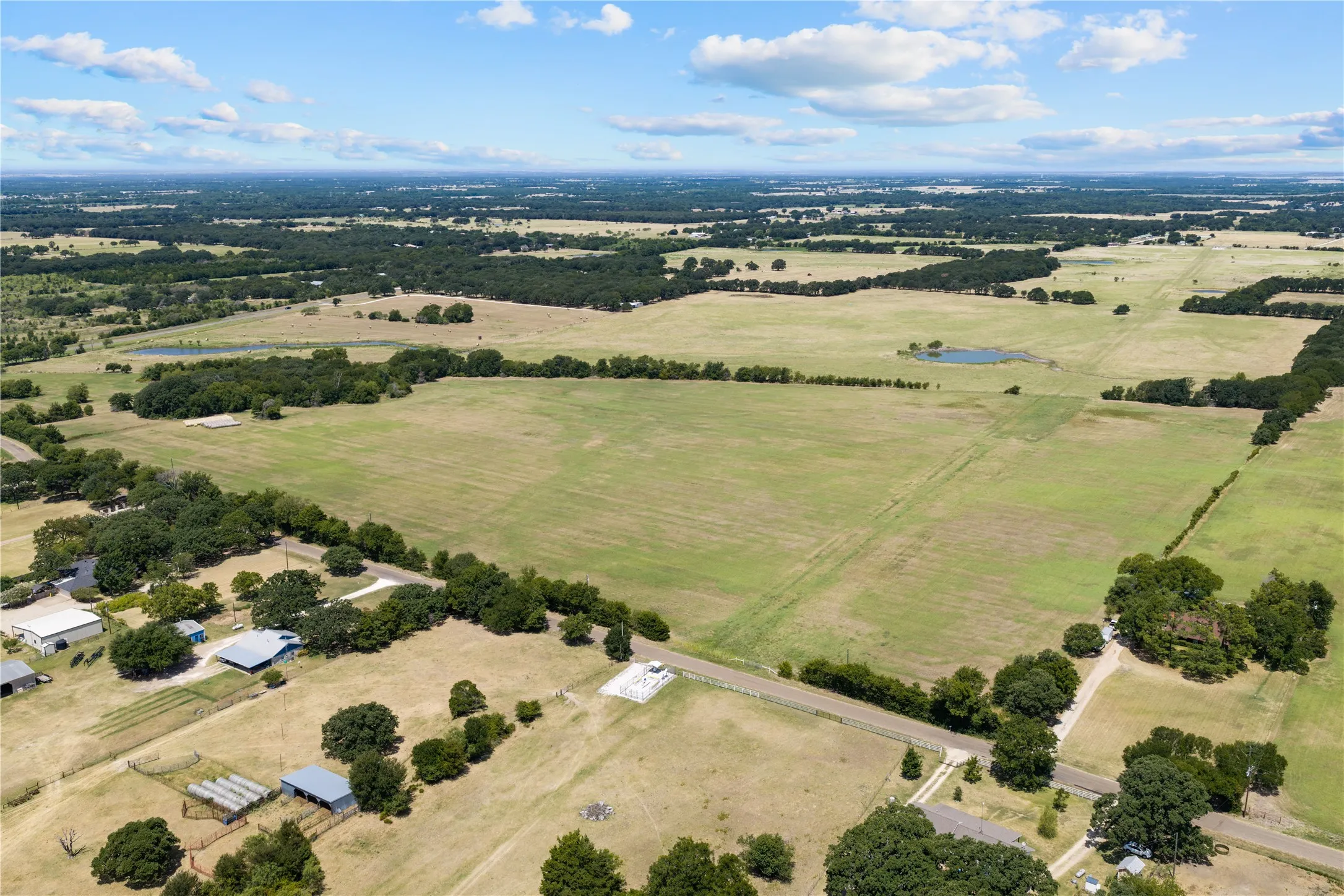 Expansive land featuring agricultural fields, mature trees, a private pond, and multiple structures