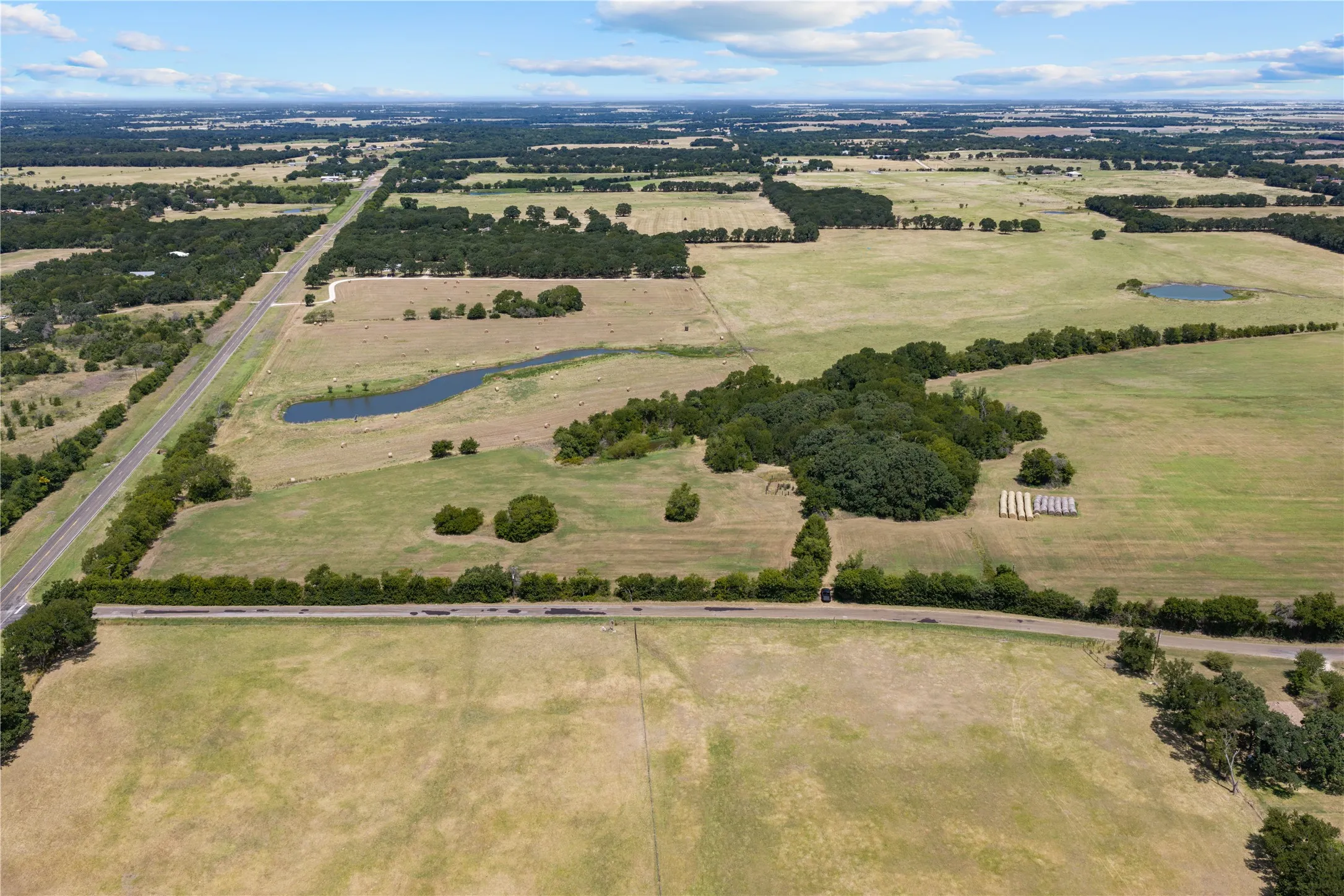 Expansive rural landscape featuring a paved road, scattered mature trees, and multiple natural ponds