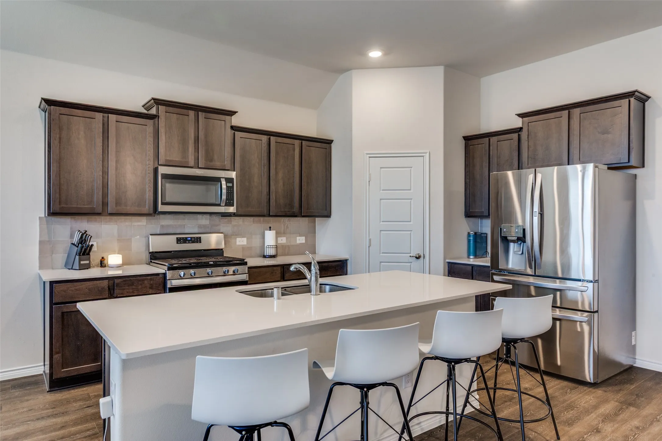 Kitchen featuring stainless steel appliances, dark wood finish cabinetry, dark wood finished floors, and a center island with sink