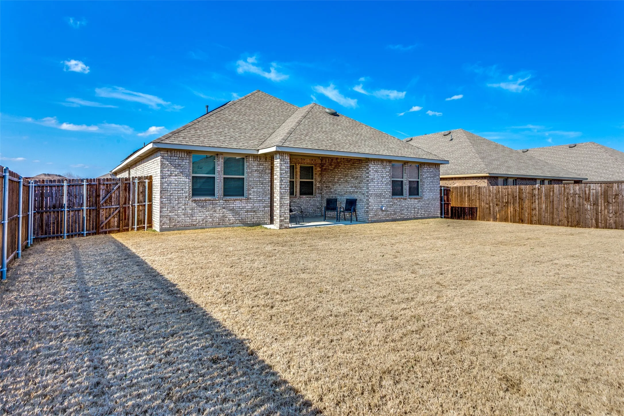 Rear view of property with a shingled roof, a patio area, a fenced backyard, brick siding, and a gate