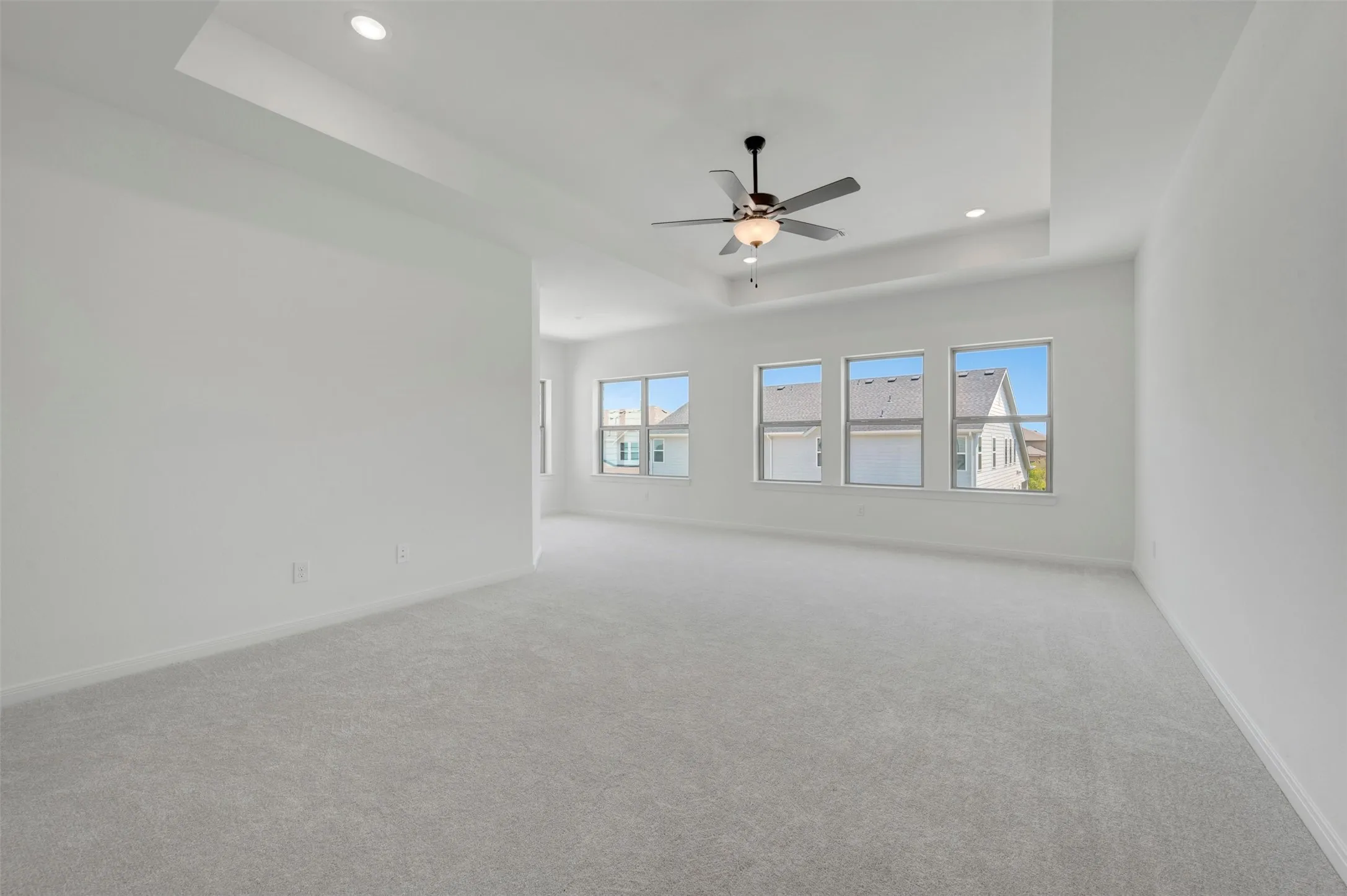 Spacious room featuring light gray carpeting, a tray ceiling, a ceiling fan with integrated lighting, and recessed lighting