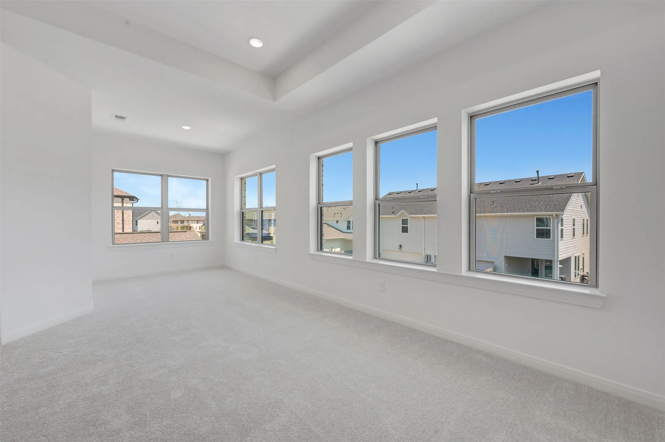 Recessed lighting, tray ceiling, multiple windows, and light-toned carpeting
