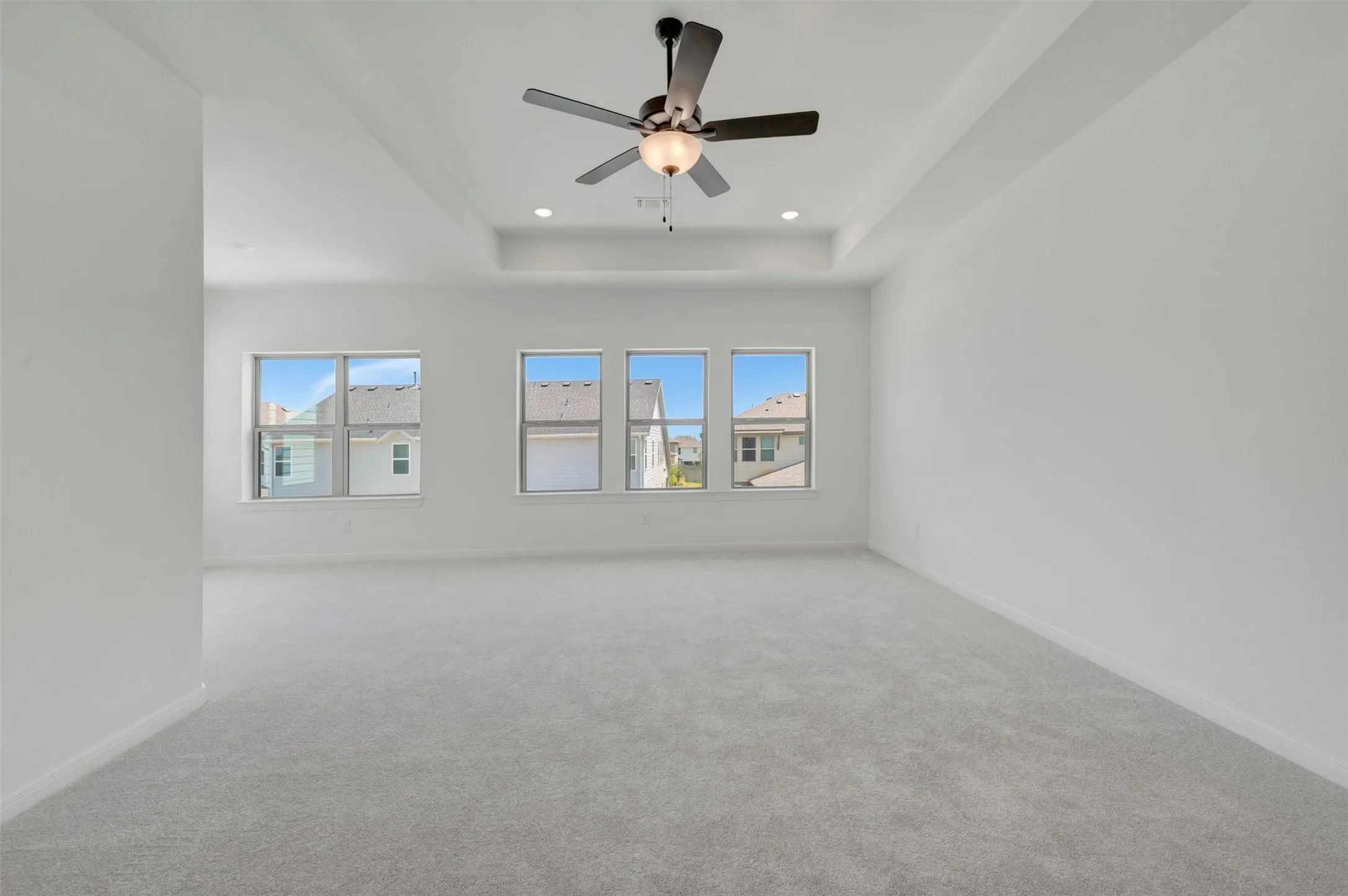 Spacious room featuring light-colored carpet, multiple windows, a tray ceiling, and a ceiling fan with integrated lighting