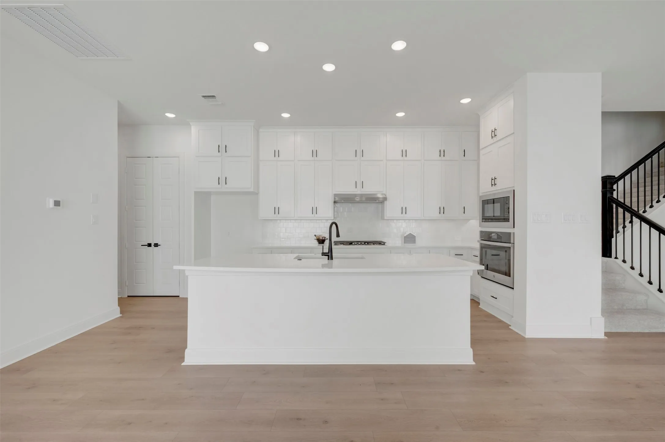 White cabinetry with dark hardware, built-in stainless steel appliances, kitchen island with sink, recessed lighting, and wood-finish flooring