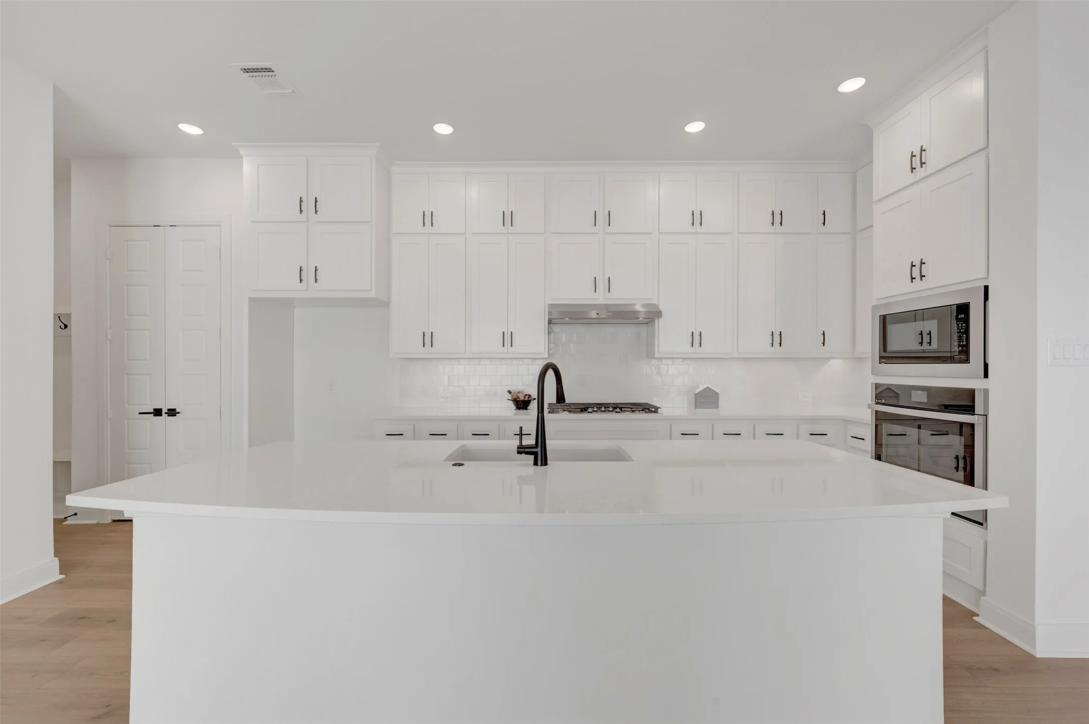Modern kitchen featuring white shaker-style cabinetry with chrome hardware, a large white quartz island with waterfall edge, stainless steel dual wall ovens, and a black gooseneck faucet over the sink