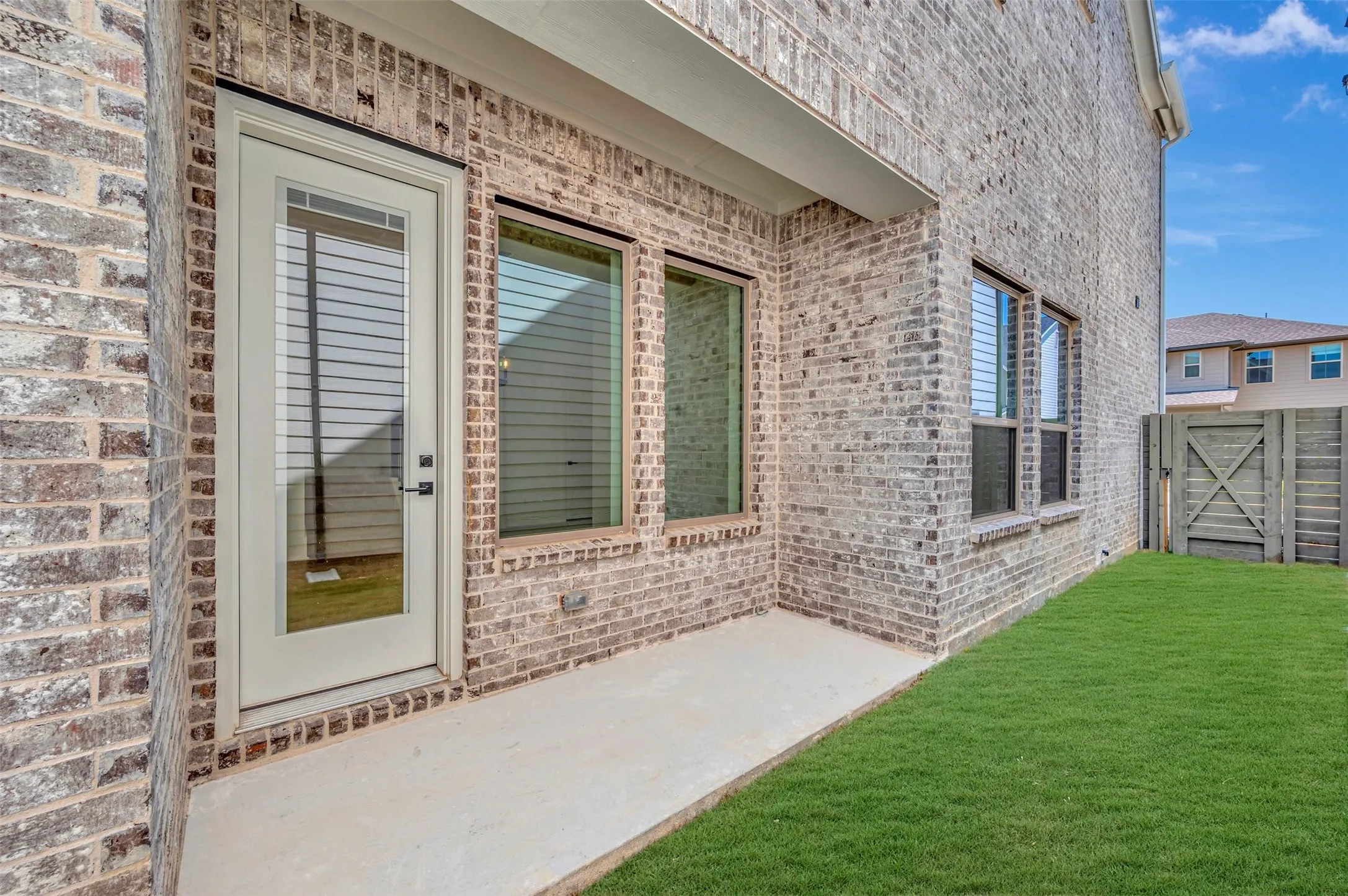 Modern brick exterior with elegant glass-panel entry door and expansive sliding glass doors opening to a manicured lawn