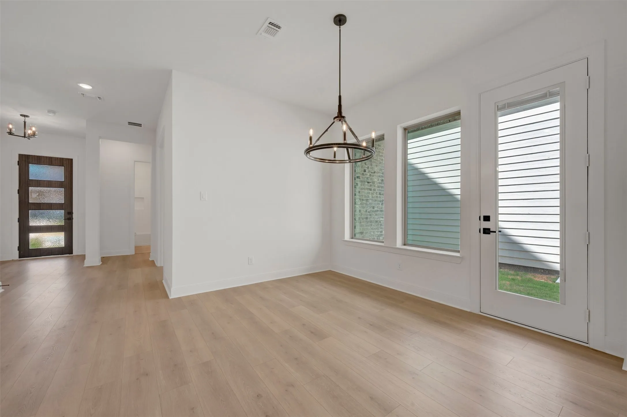 Open-concept living area featuring wood-finish flooring, a modern chandelier, and a white paneled door with glass inserts