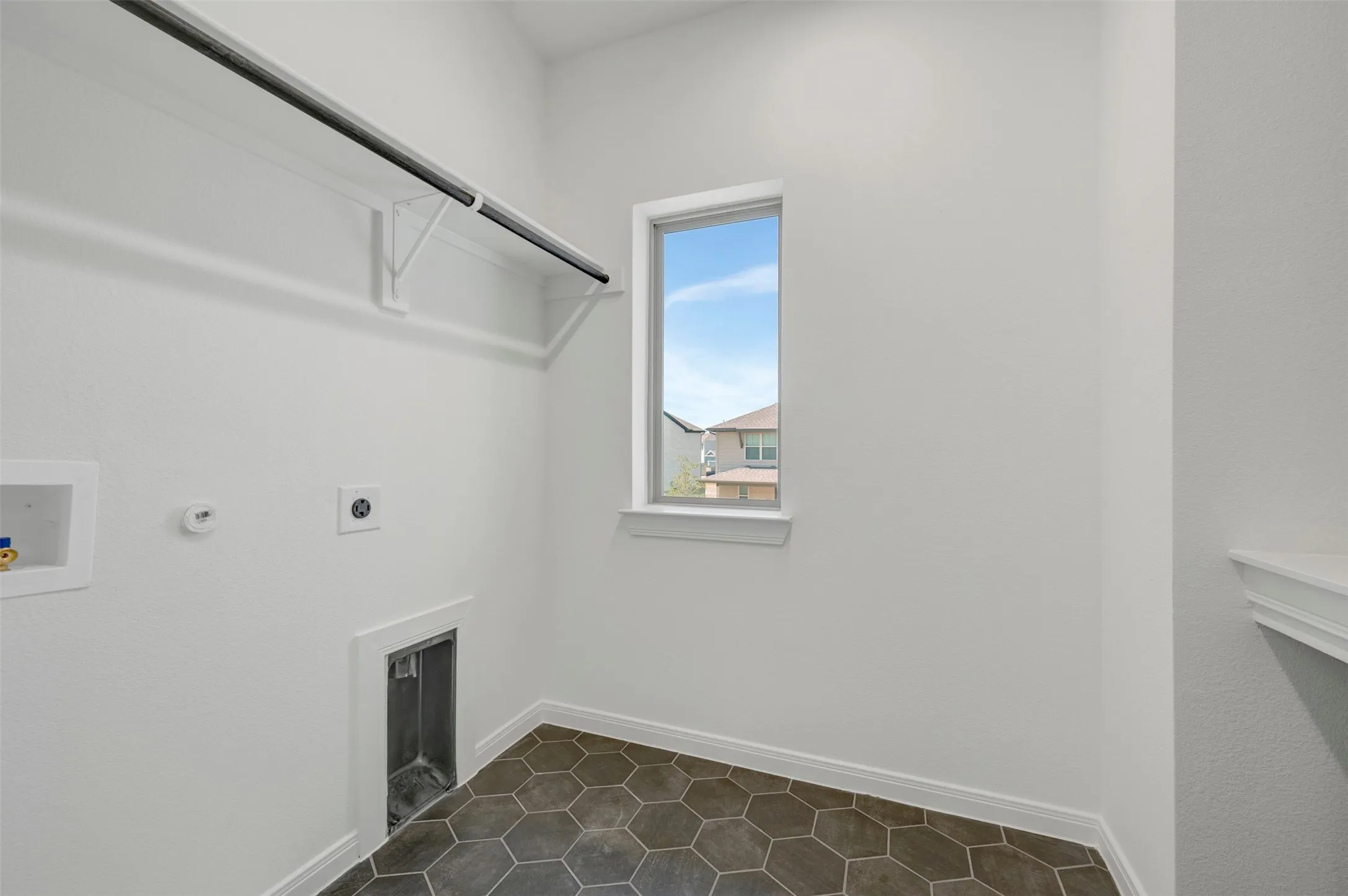 Laundry area featuring hexagonal floor tiles, a single window, an integrated clothes rod, and white wall finishes