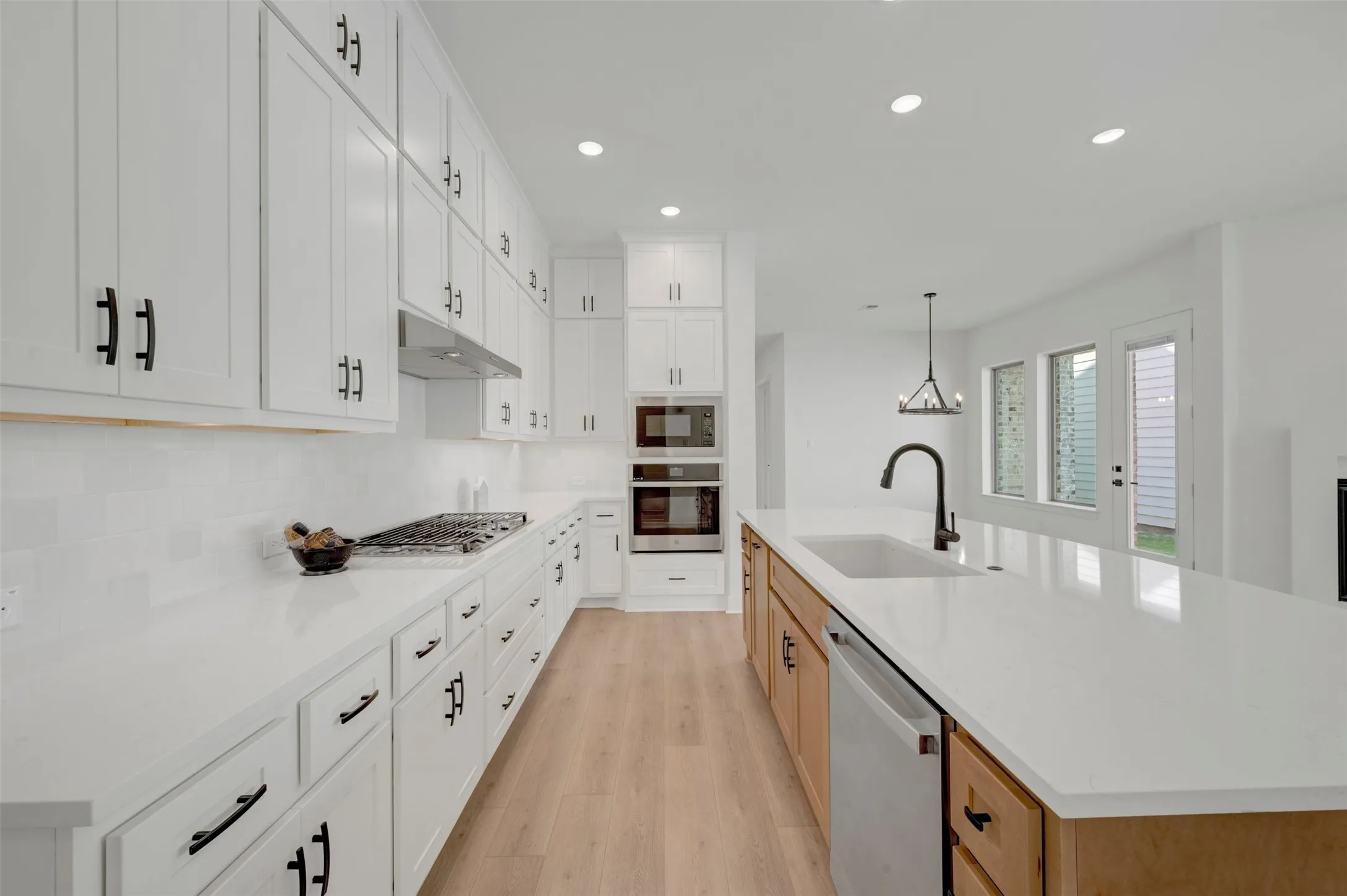 Gourmet kitchen featuring extensive white cabinetry, quartz countertops, wood-finish flooring, a stainless steel gas range, and a kitchen island with an undermount sink