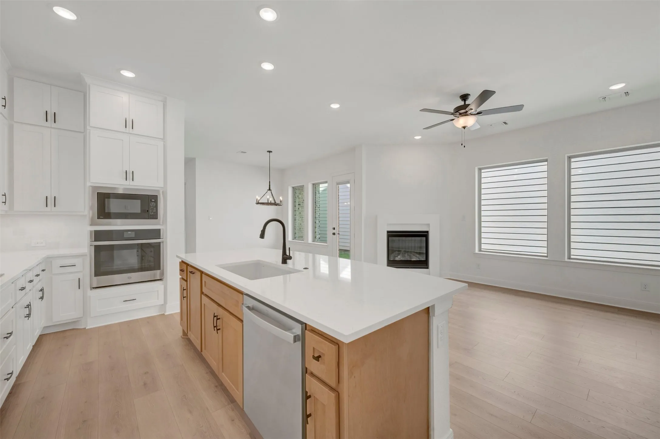 Open-concept design featuring wood-finish flooring, a kitchen island with a built-in sink and dishwasher, white upper cabinetry, and a fireplace