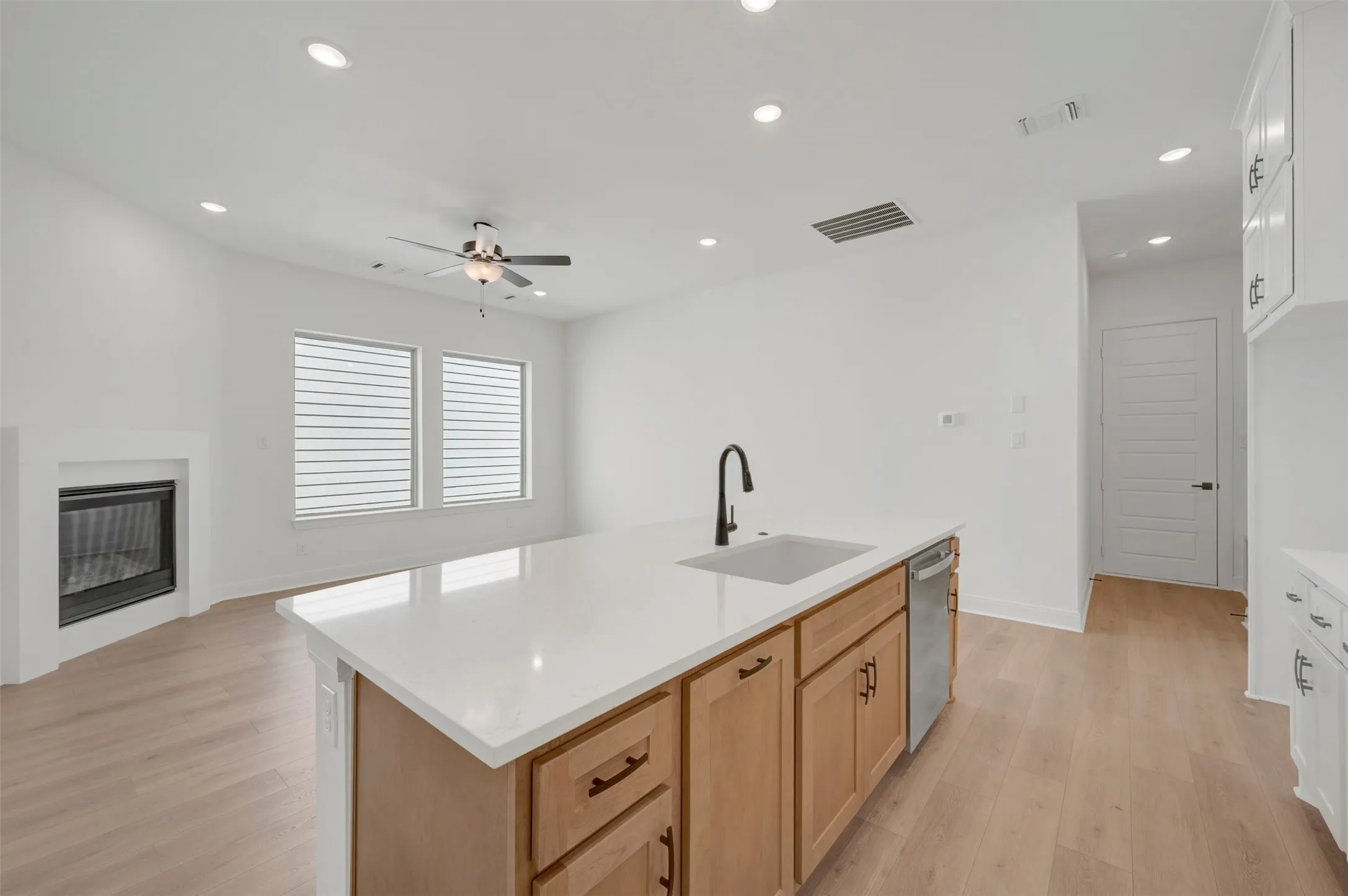 Kitchen island with a light-toned countertop and wood-finish cabinetry, a stainless steel dishwasher, and a black faucet with an undermount sink