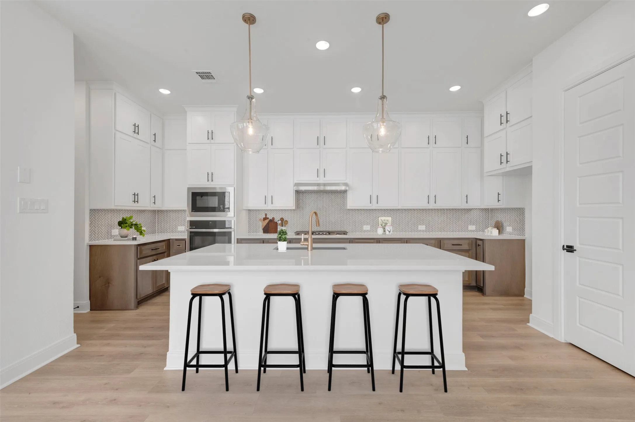 Chef's kitchen showcasing a large white waterfall-edge island with seating for four, white shaker cabinetry with brushed metal hardware, stainless steel appliances, subway tile backsplash, pendant lighting with brass accents, and wood-finish flooring throughout the open layout