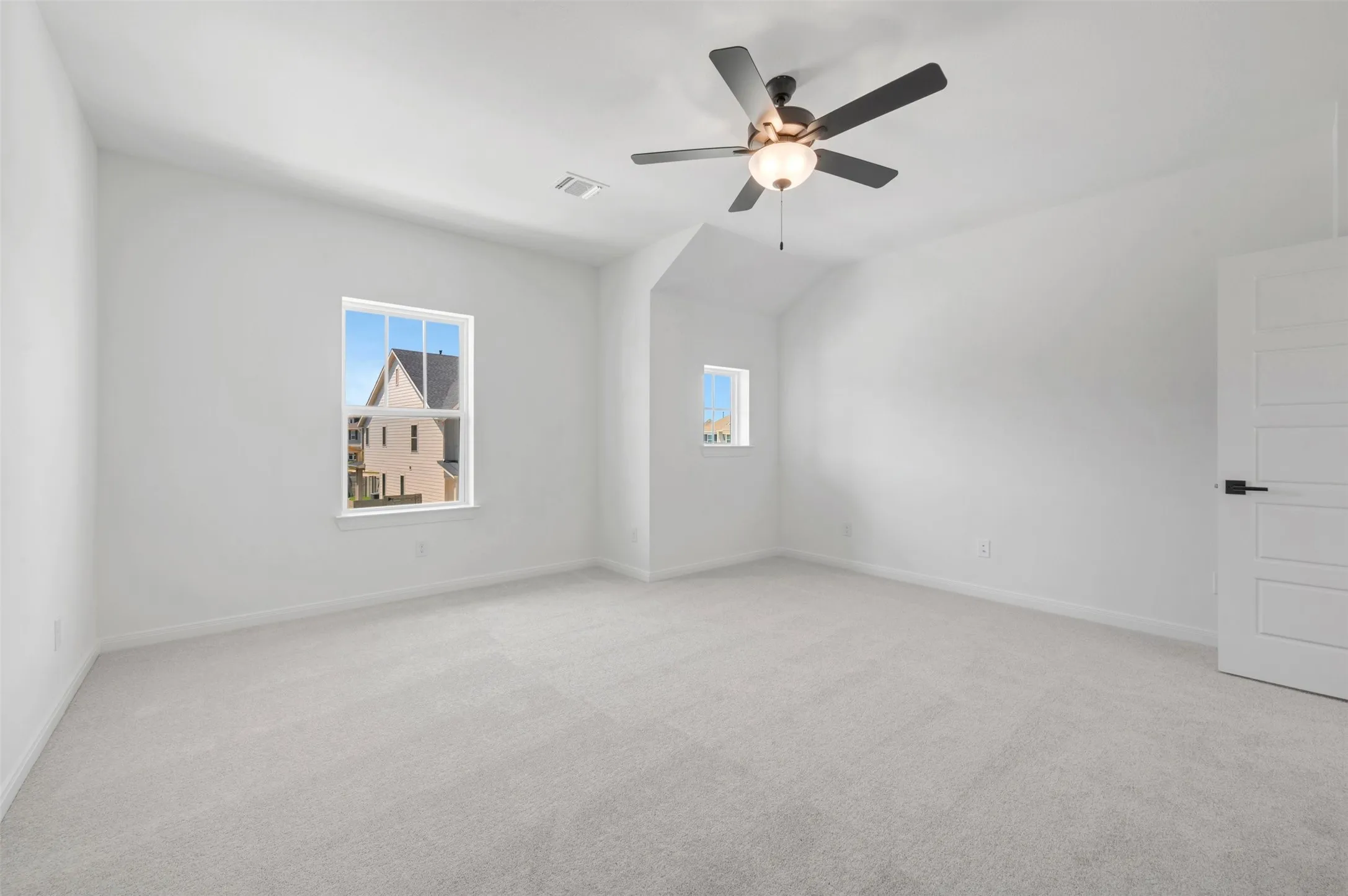 Bright, light-filled bedroom showcasing neutral carpeting, a ceiling fan with integrated lighting, and dual windows framing natural light throughout the space