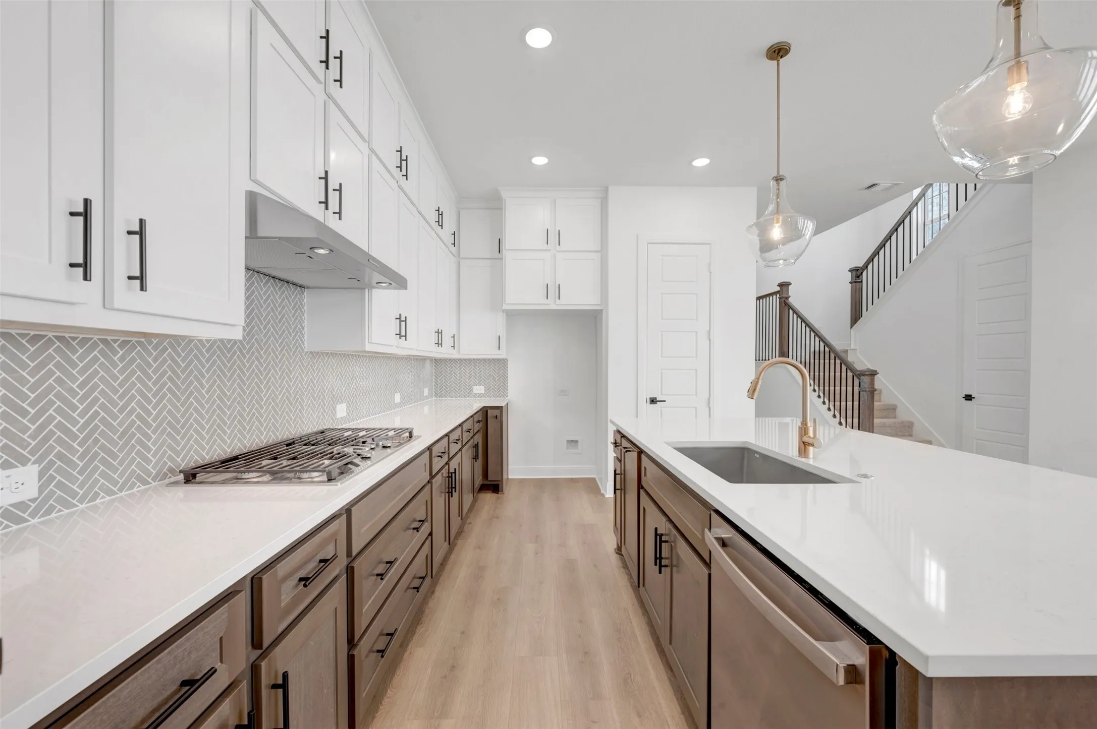 Chef's kitchen featuring white cabinetry with brushed metal hardware, white quartz countertops, a herringbone tile backsplash, stainless steel gas cooktop, and a large center island with waterfall-edge countertop and pendant lighting