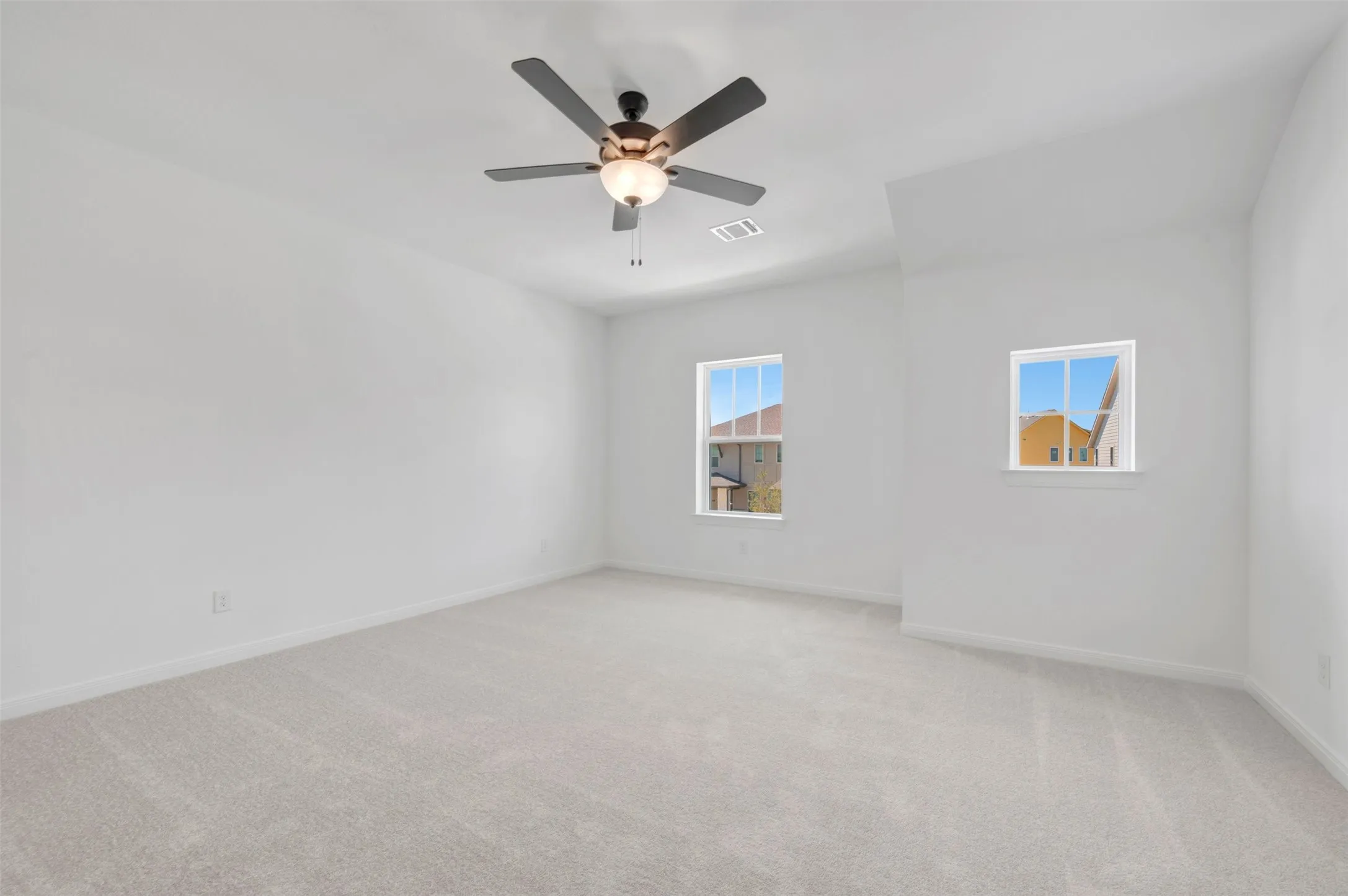 Spacious room featuring light-colored carpeting, multiple windows, a ceiling fan with integrated lighting, and crisp white walls