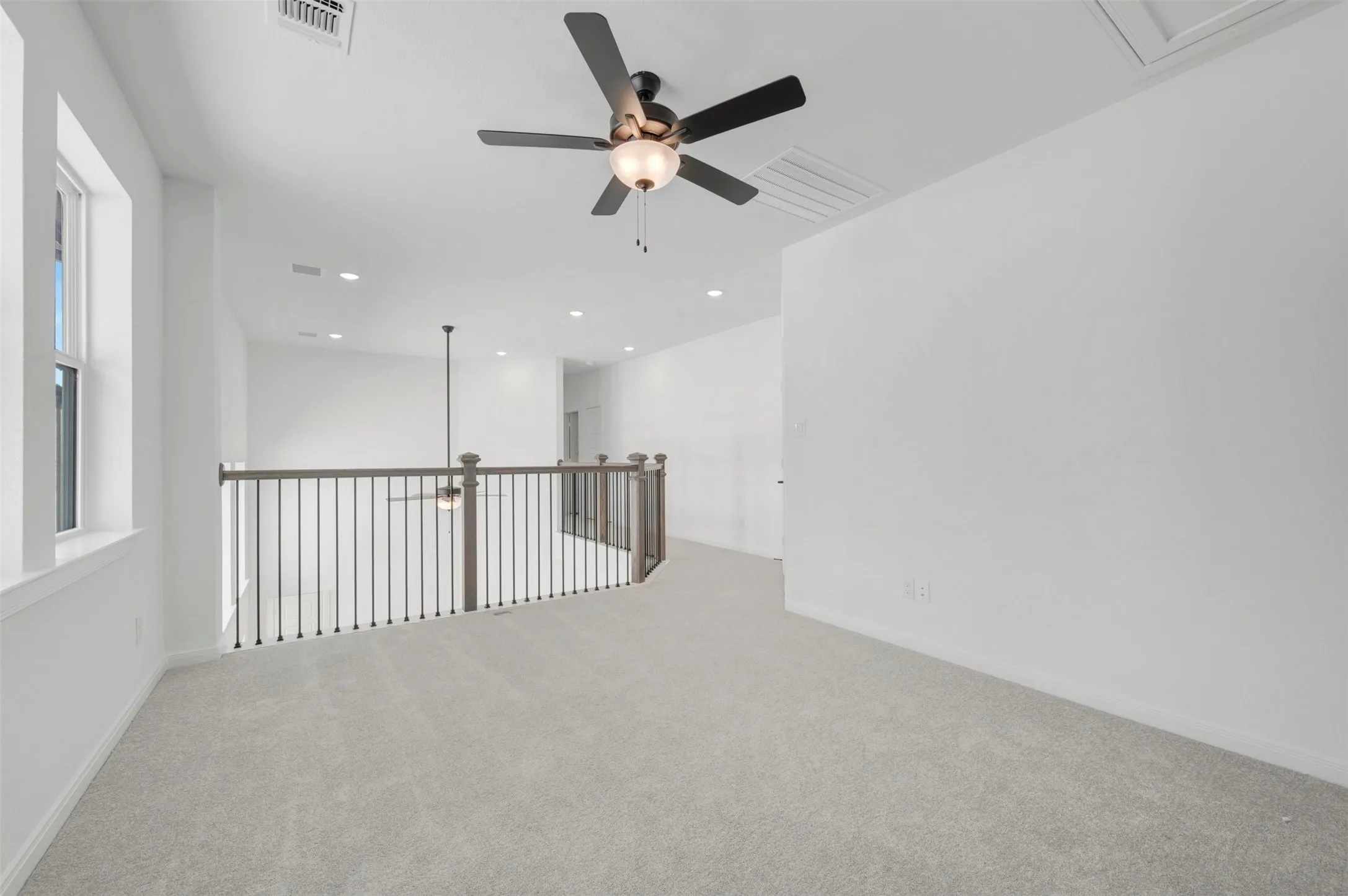 Carpeted loft area featuring a ceiling fan, recessed lighting, a window, and a wooden railing with vertical balusters