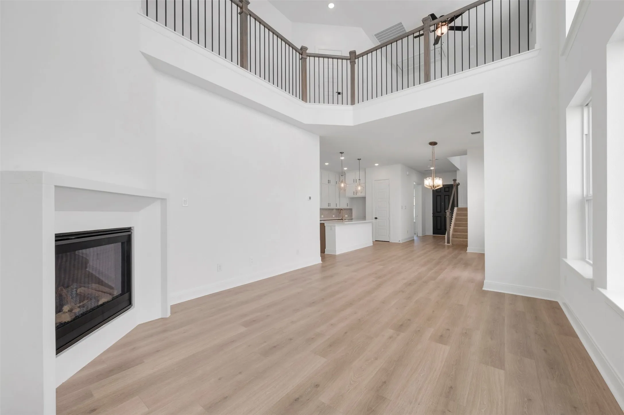 Spacious interior featuring high ceilings, light wood-finish flooring, a built-in fireplace, and an open balcony with dark iron balusters