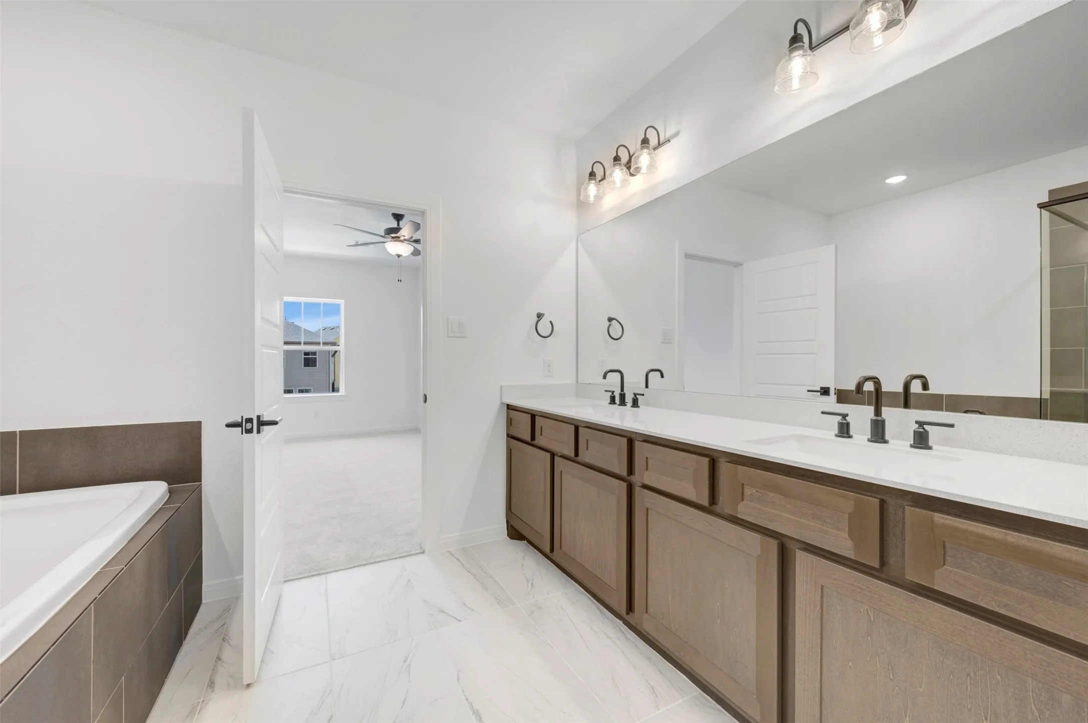 Spa-inspired primary bathroom featuring a wood-finish dual vanity with white quartz countertops, dual vessel sinks with oil-rubbed bronze faucets, and an illuminated mirror