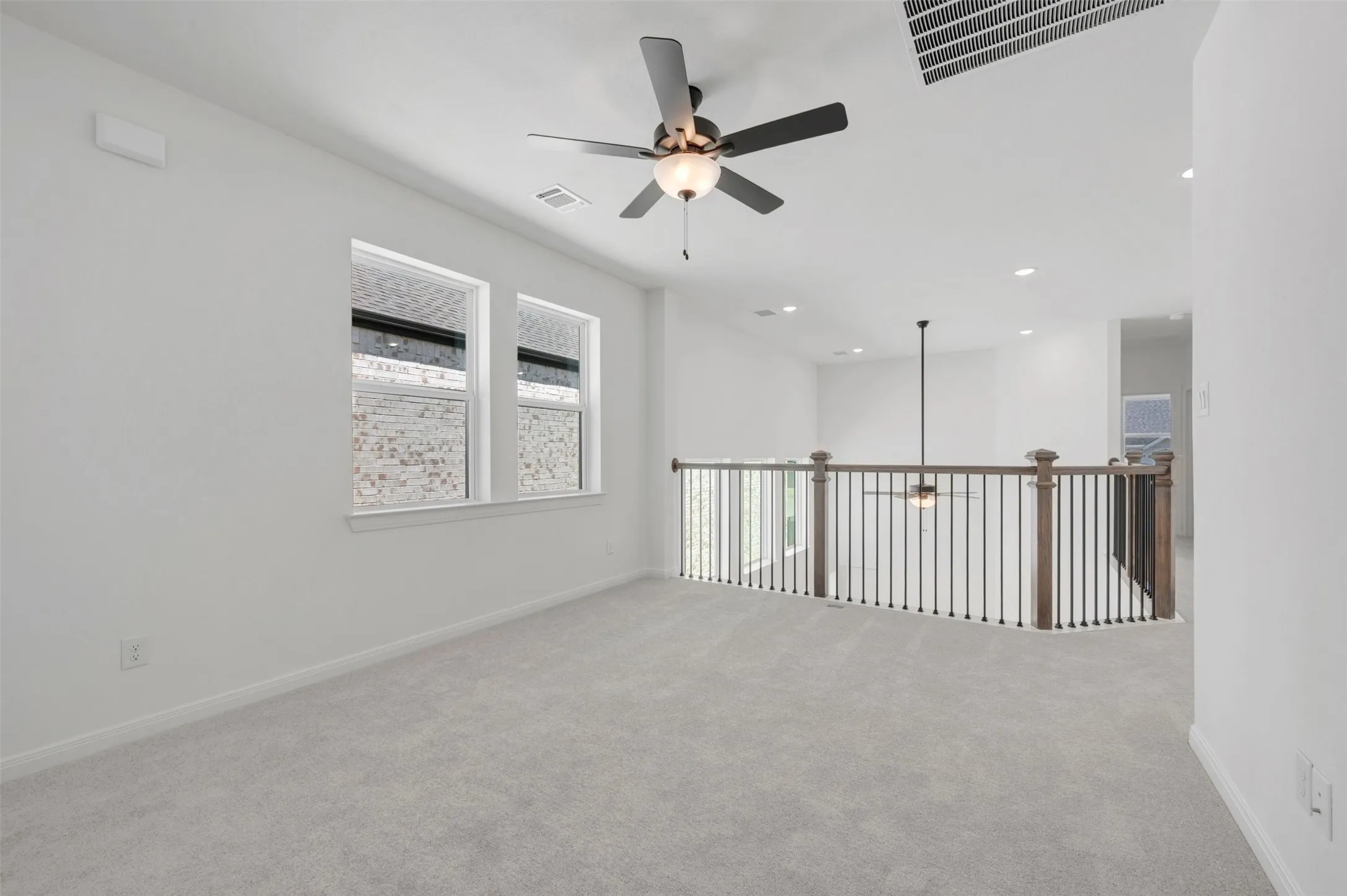Spacious loft-style room featuring neutral carpet flooring, recessed lighting, and a ceiling fan with integrated light fixture