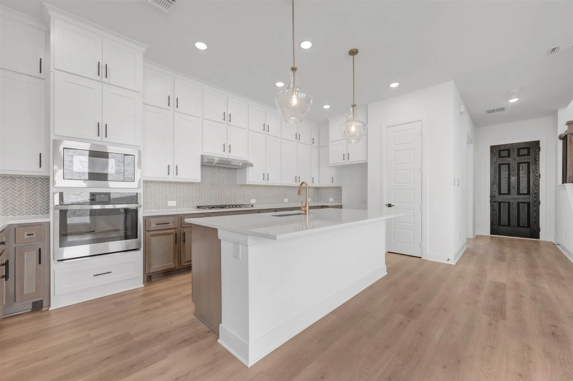 White shaker cabinetry, stainless steel appliances, herringbone tile backsplash, a center island with countertop seating, and wood-finish flooring